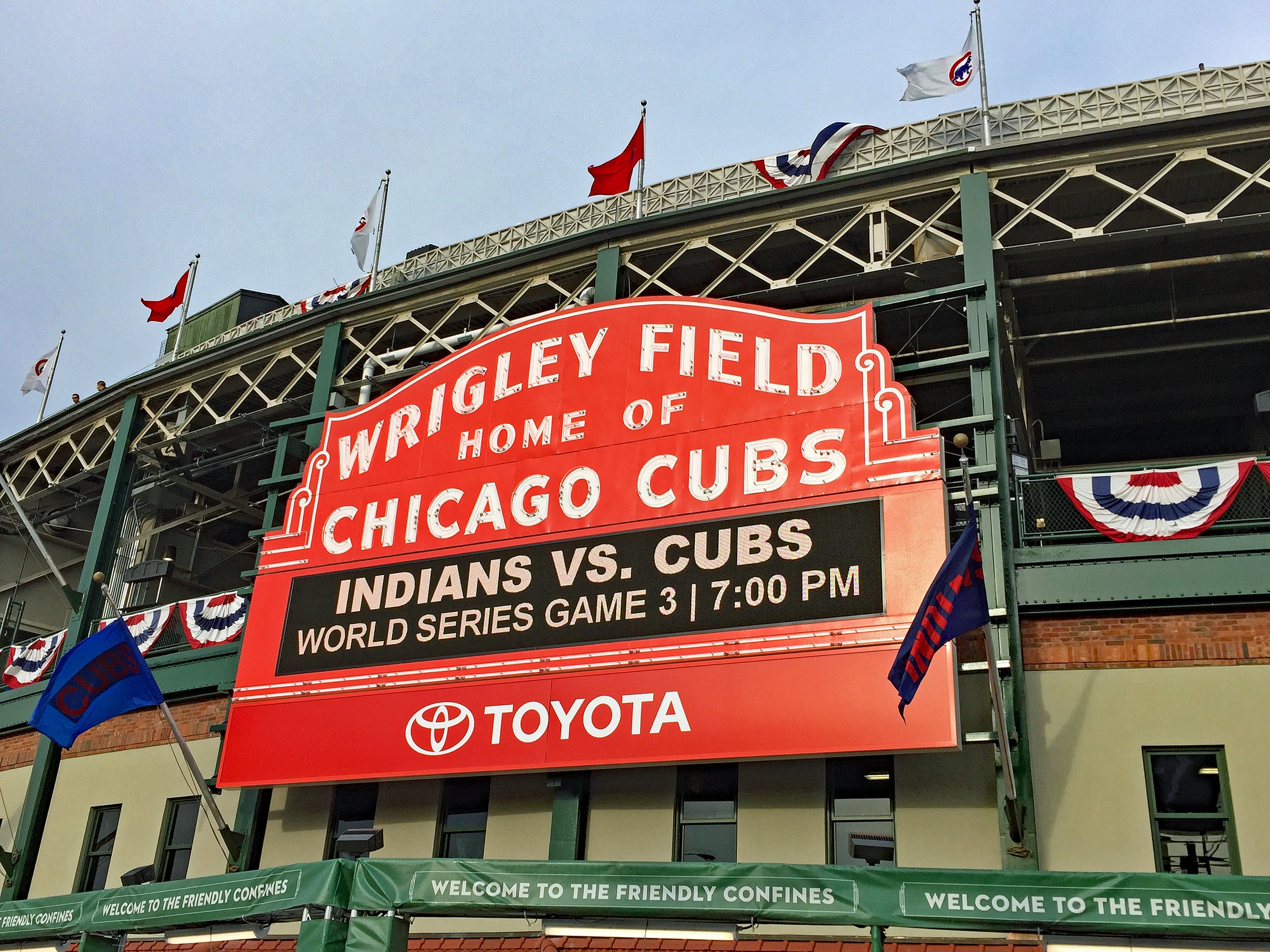 View of Wrigley Field entrance with flags and banners, showing the sign for a game between the Chicago Cubs and the Indiana team, with decorations in red, white, and blue for the World Series.