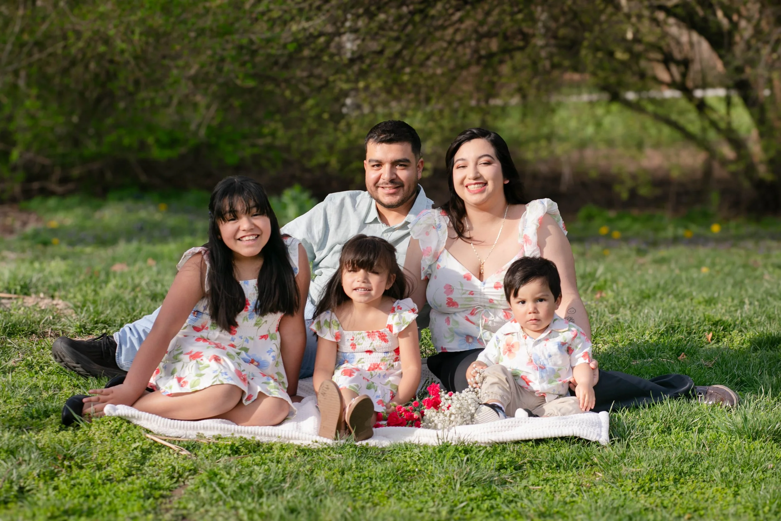 Hispanic family sitting on blanket on grass, wearing floral clothing in springtime in Omaha Nebraska