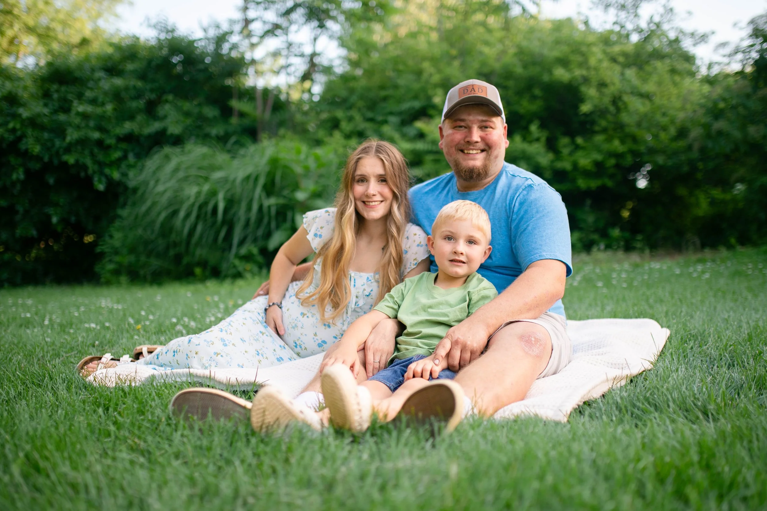 Family sitting on white blanket on grass smiling at camera in summer in Omaha Nebraska