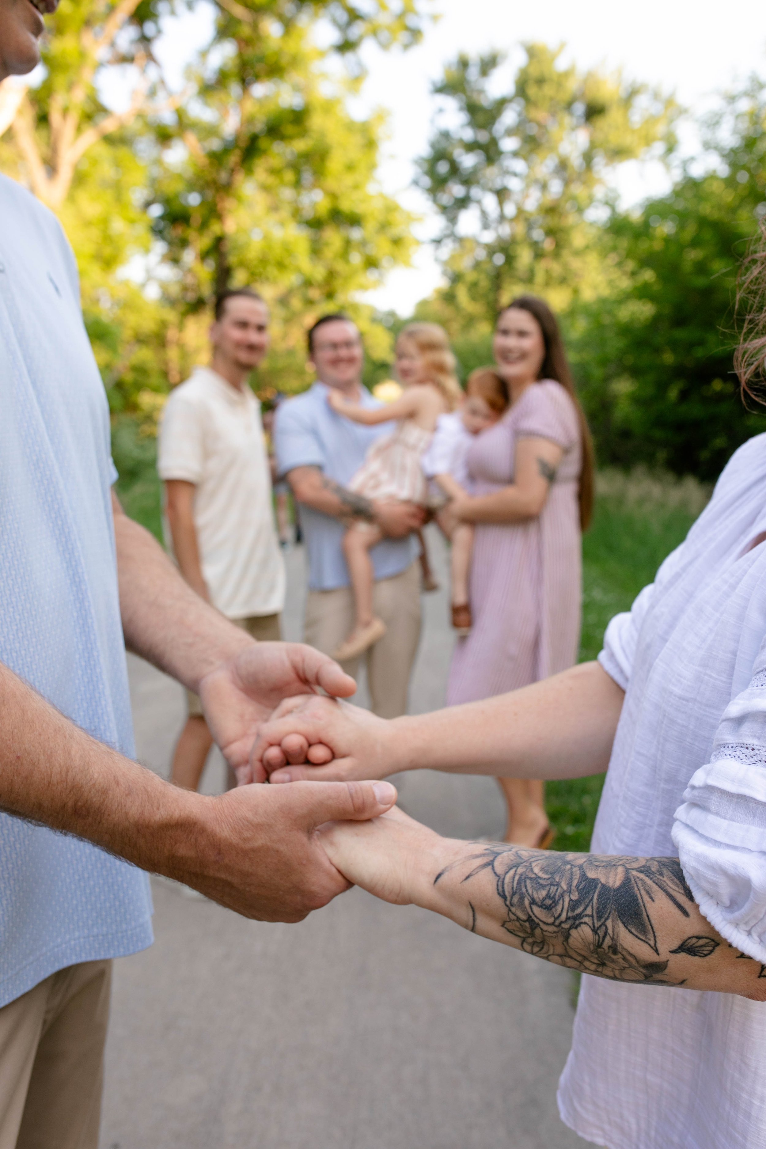 Man and woman holding hands in forefront of photo with adult children and grandchildren in the blurred background smiling at camera