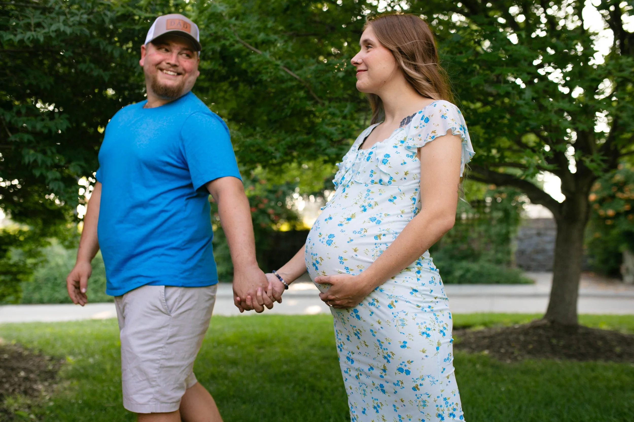 Man and pregnant woman in coordinating blue and white outfits holding hands walking in summer in Omaha Nebraska