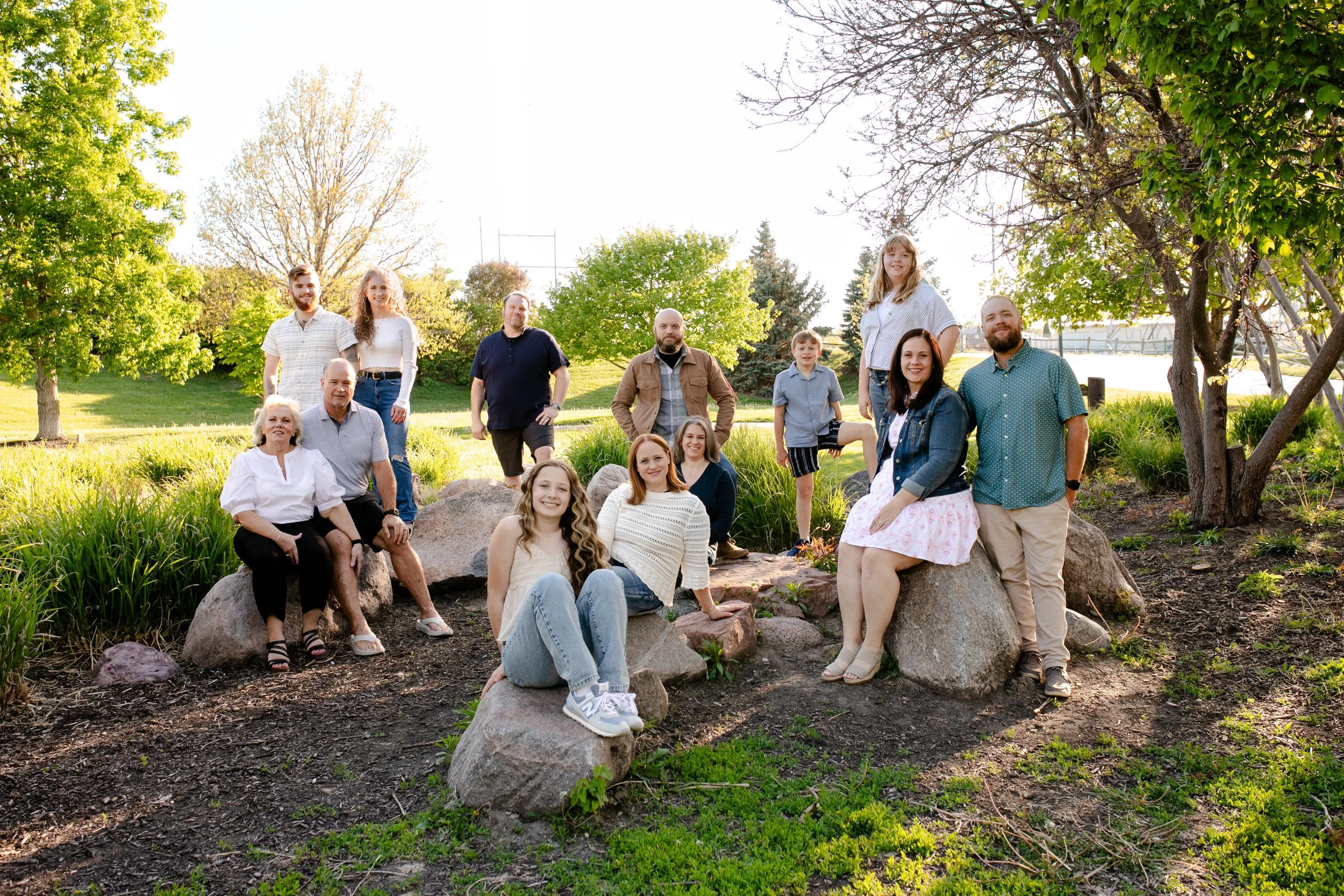 Extended family sitting and standing on large rocks in grassy arboretum in Omaha Nebraska