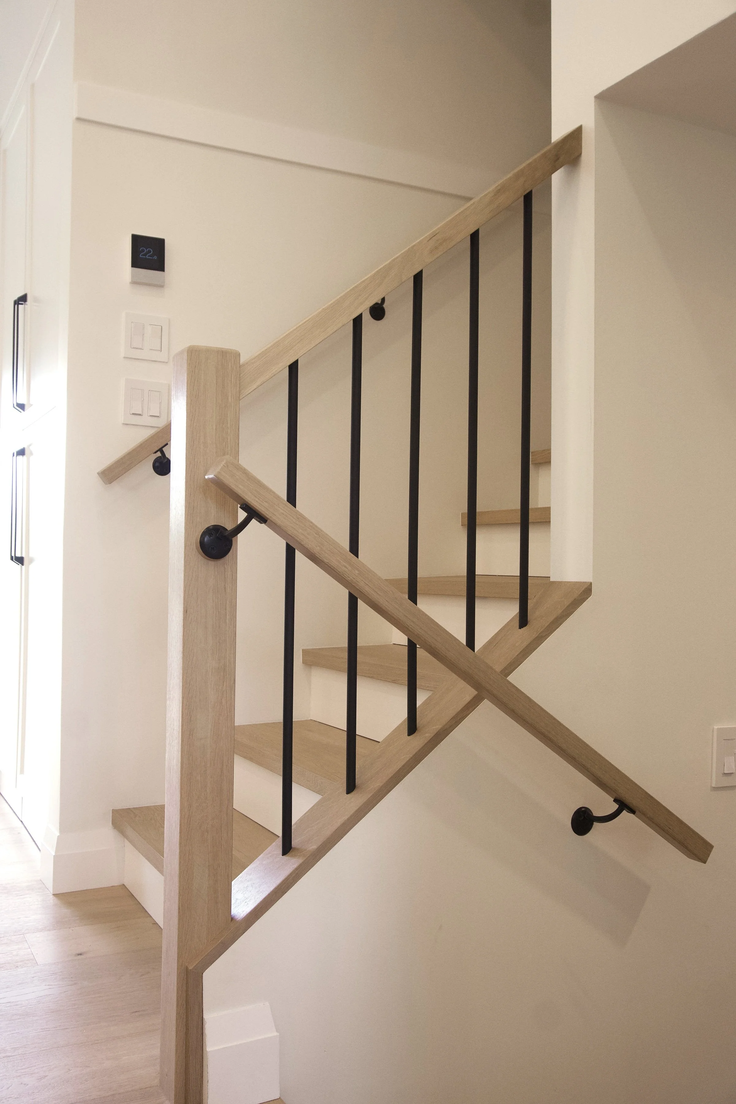White oak handrail mounted to newel post. Round black iron spindles. 