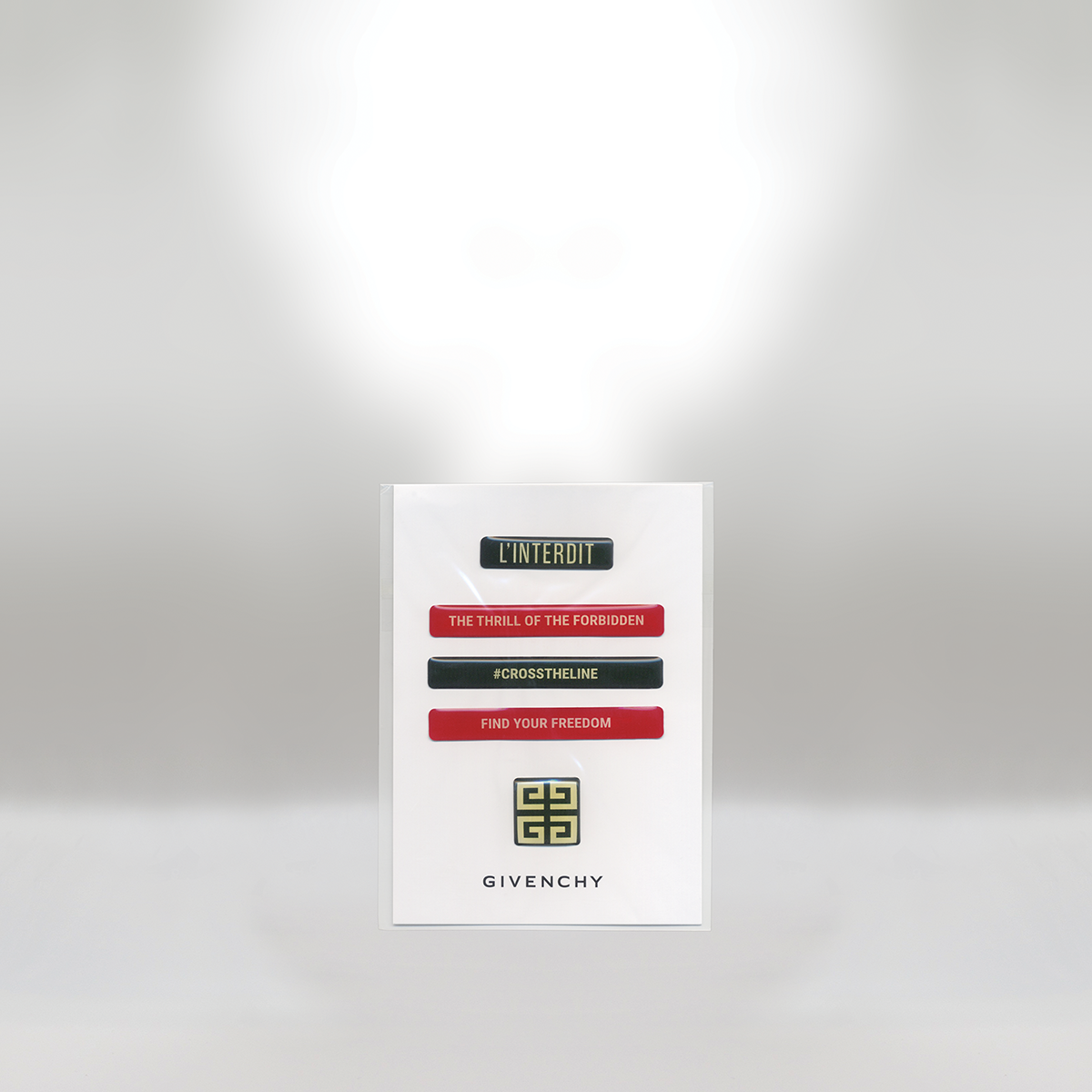 A white poster with the Givenchy logo and text in black, red, and green. The text reads: 'L'INTERDIT,' 'THE THRILL OF THE FORBIDDEN,' '#CROSSTHELENE,' and 'FIND YOUR FREEDOM.'