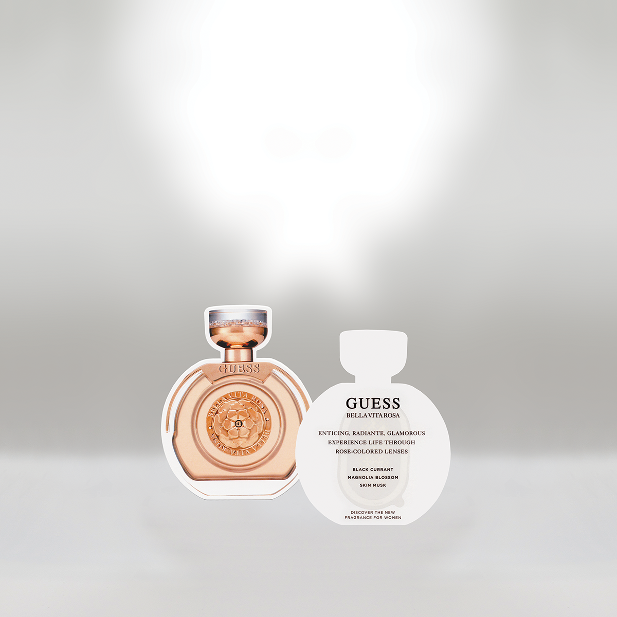 A Guess Bella Vita Rosa perfume bottle and a perfume sample card on a plain gray background.