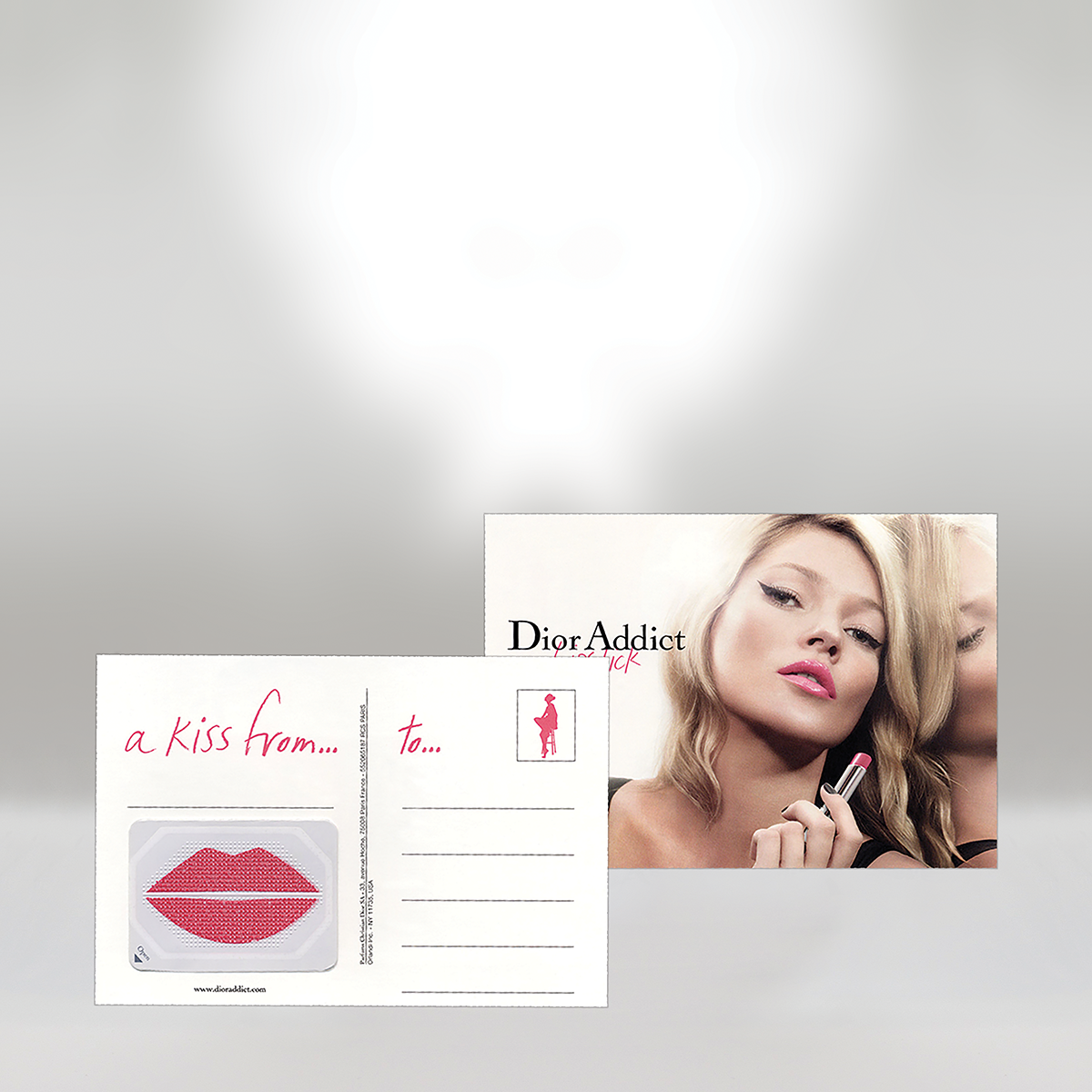 Publicité pour le rouge à lèvres Dior Addict représentant une femme aux cheveux blonds appliquant un rouge à lèvres rose, une carte-cadeau avec des lèvres rouges et un message manuscrit "un baiser de... à...", ainsi que la marque Dior Addict.