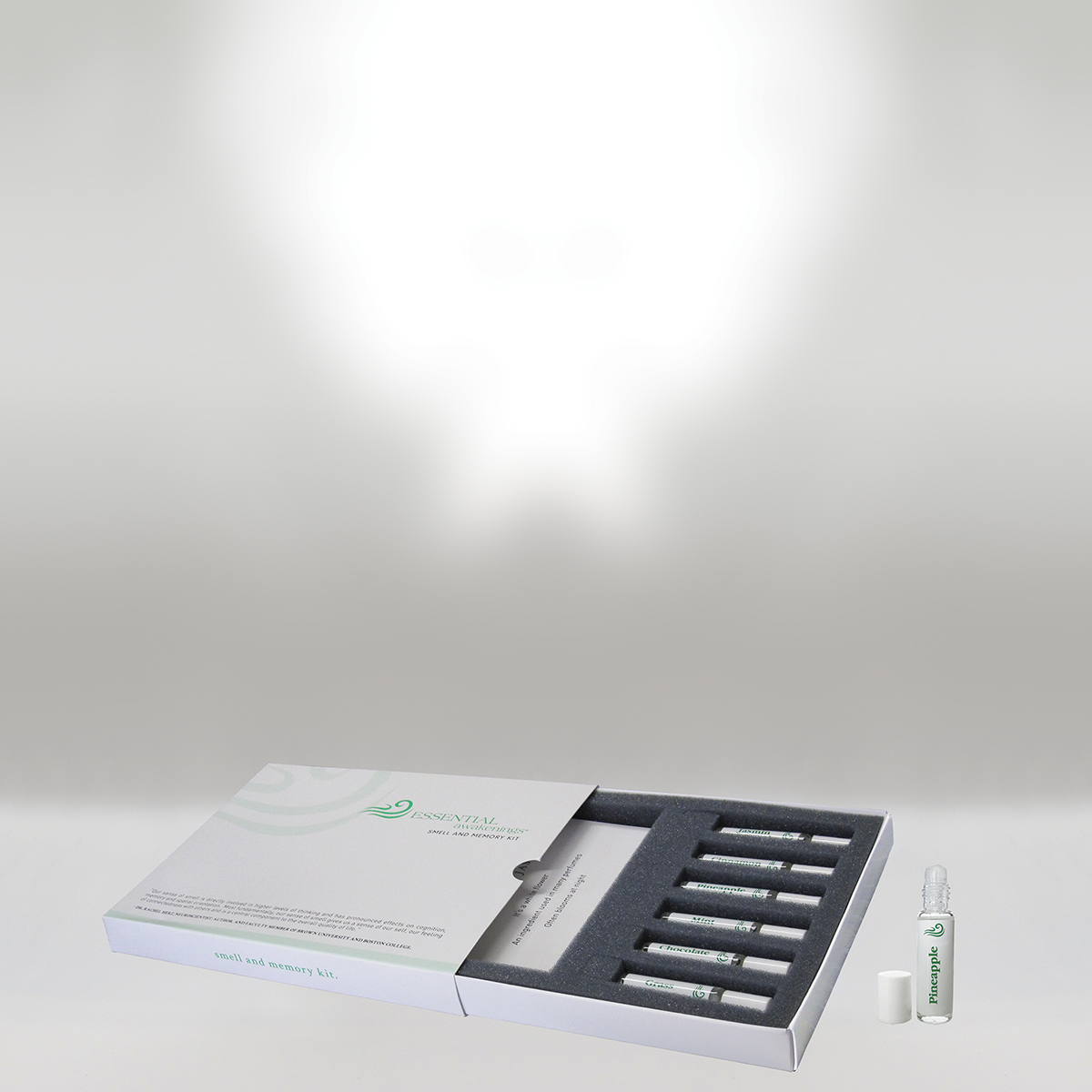 A smell and memory kit with a white box containing eight small vials, one labeled pineapple, with a white cap beside it, on a white surface.
