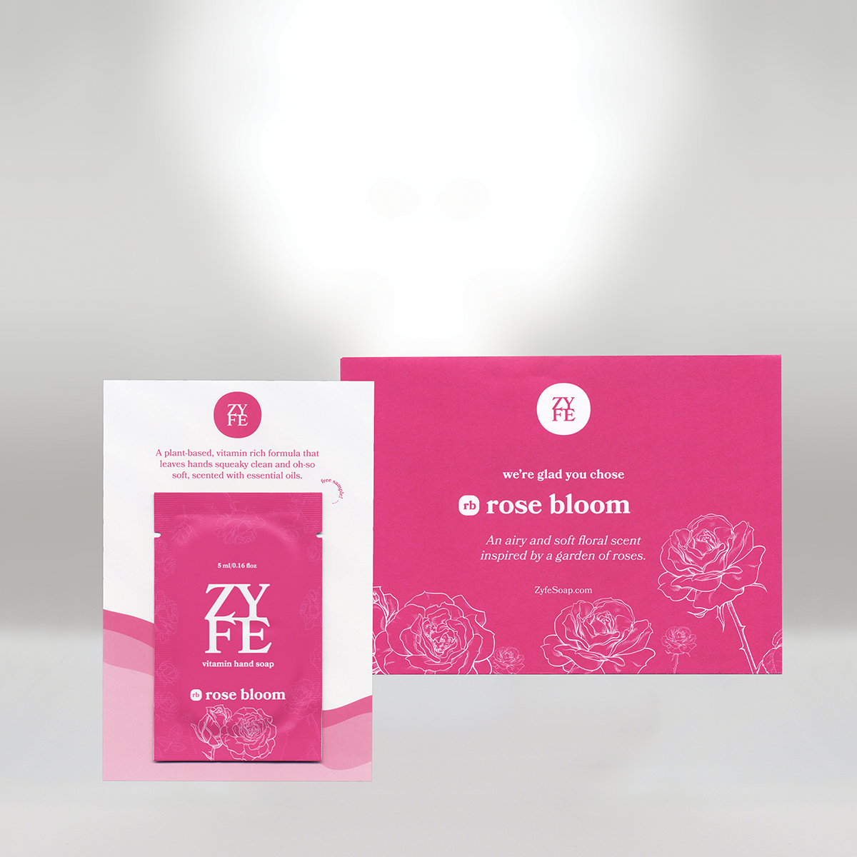 Pink and white sample packet and business card for Zyfe Rose Bloom hand soap, featuring rose illustrations and product description, on a light gray background.