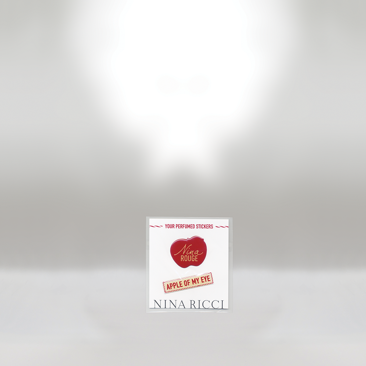 Perfumed sticker with a red apple graphic and gold script that says "Nina Rouge," a stencil-style red text "Apple of My Eye," and the brand name Nina Ricci at the bottom, set against a white background.