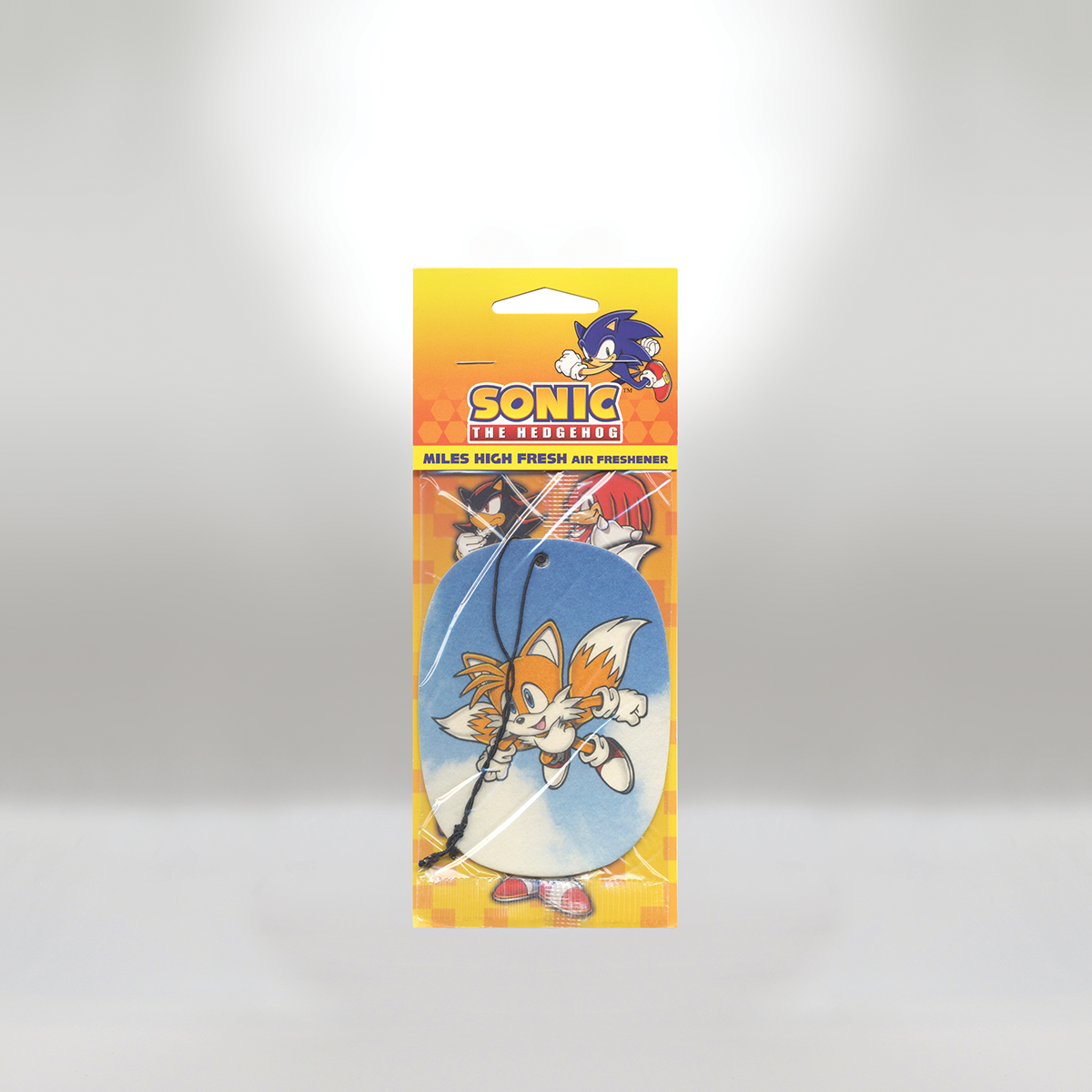 Sonic the Hedgehog air freshener with a cartoon image of Tails against a blue background, hanging on a black string. The packaging is in yellow and orange with Sonic's logo and characters in the background.