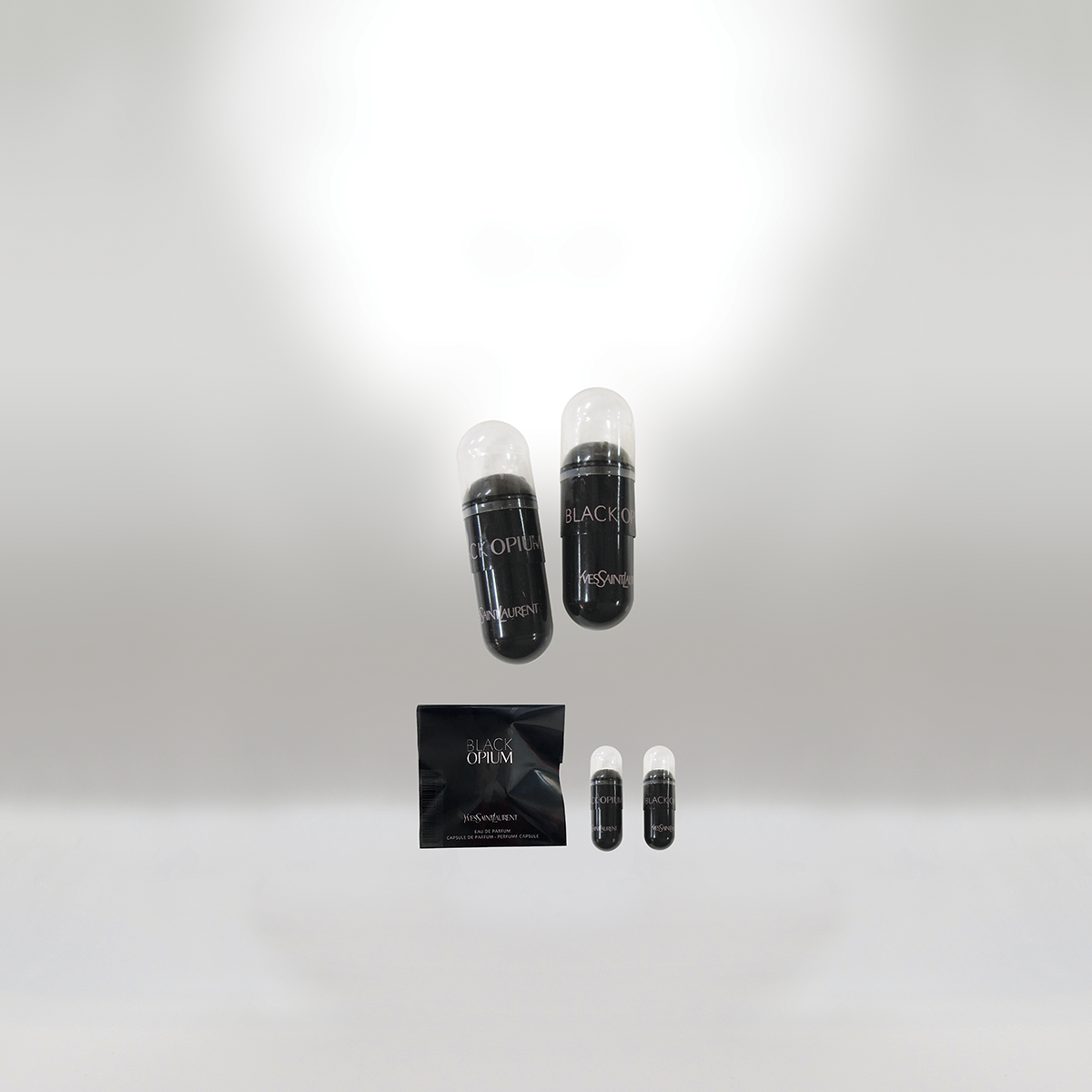 Two capsule-shaped perfume containers labeled 'Black Opium' by Yves Saint Laurent, floating above a small black pouch with similar branding, against a plain, light background.