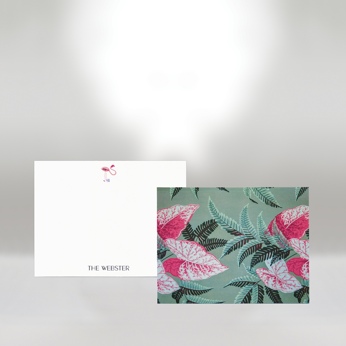 A set of two cards, one with a pink flamingo and a small blue and white object, and the other with pink and green leaves on a green background, placed on a white surface.