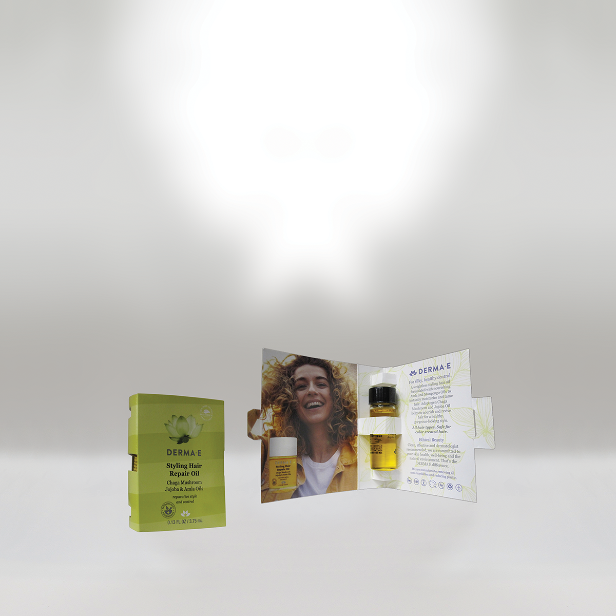 Display of Derma E Styling Hair Repair Oil with packaging and promotional booklet showcasing a smiling woman with curly hair.
