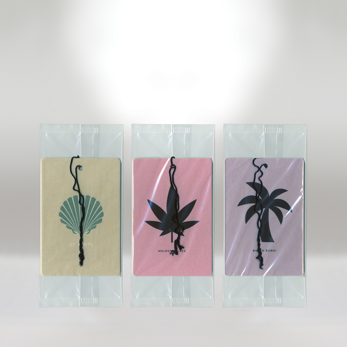 Three clear plastic packages each with a card featuring a black silhouette of a different tropical or floral design, and a black string attached.
