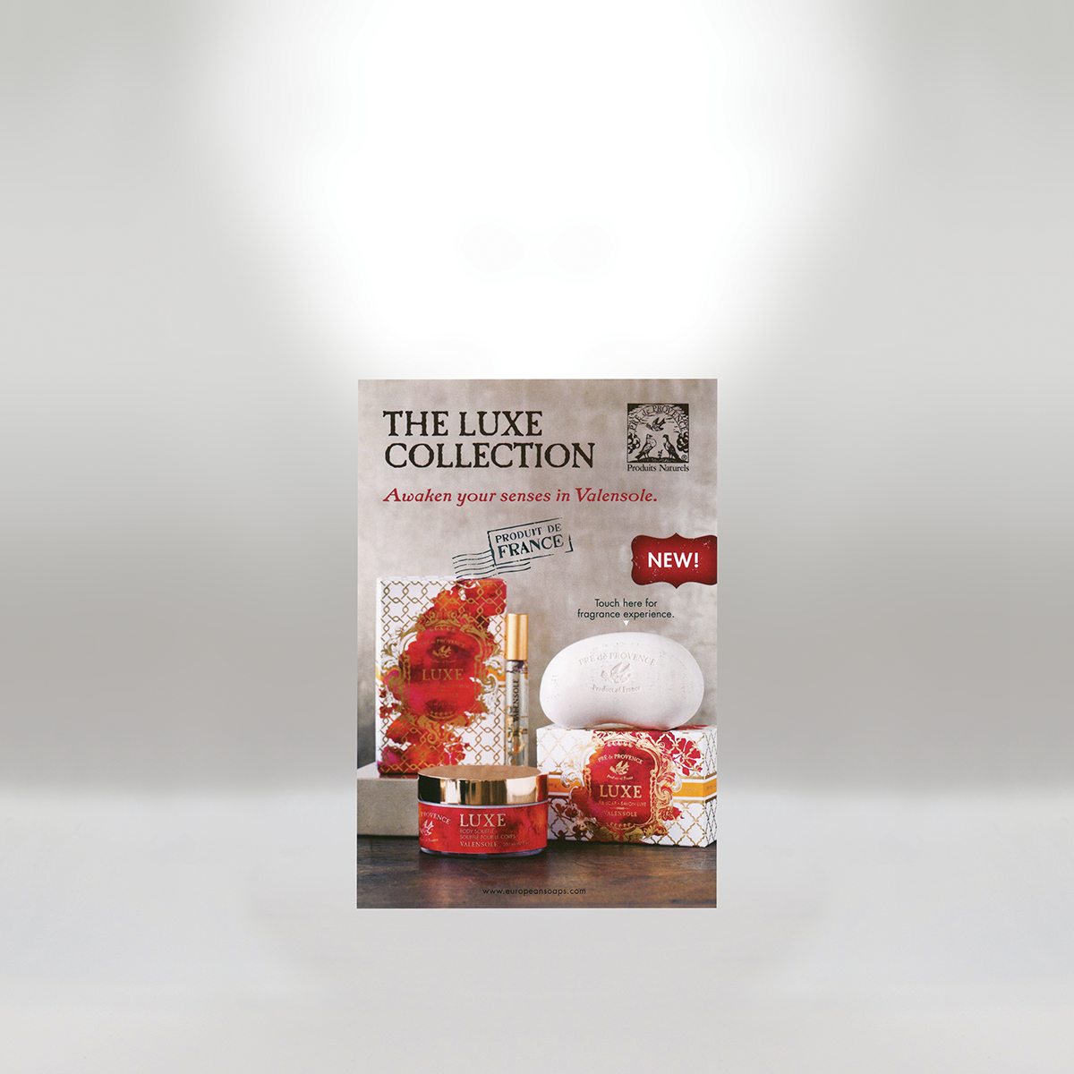 A promotional poster for The Luxe Collection of Valensole fragrance products featuring a red and gold jar, a white soap, and a small spray bottle, with text highlighting newness and French origin.