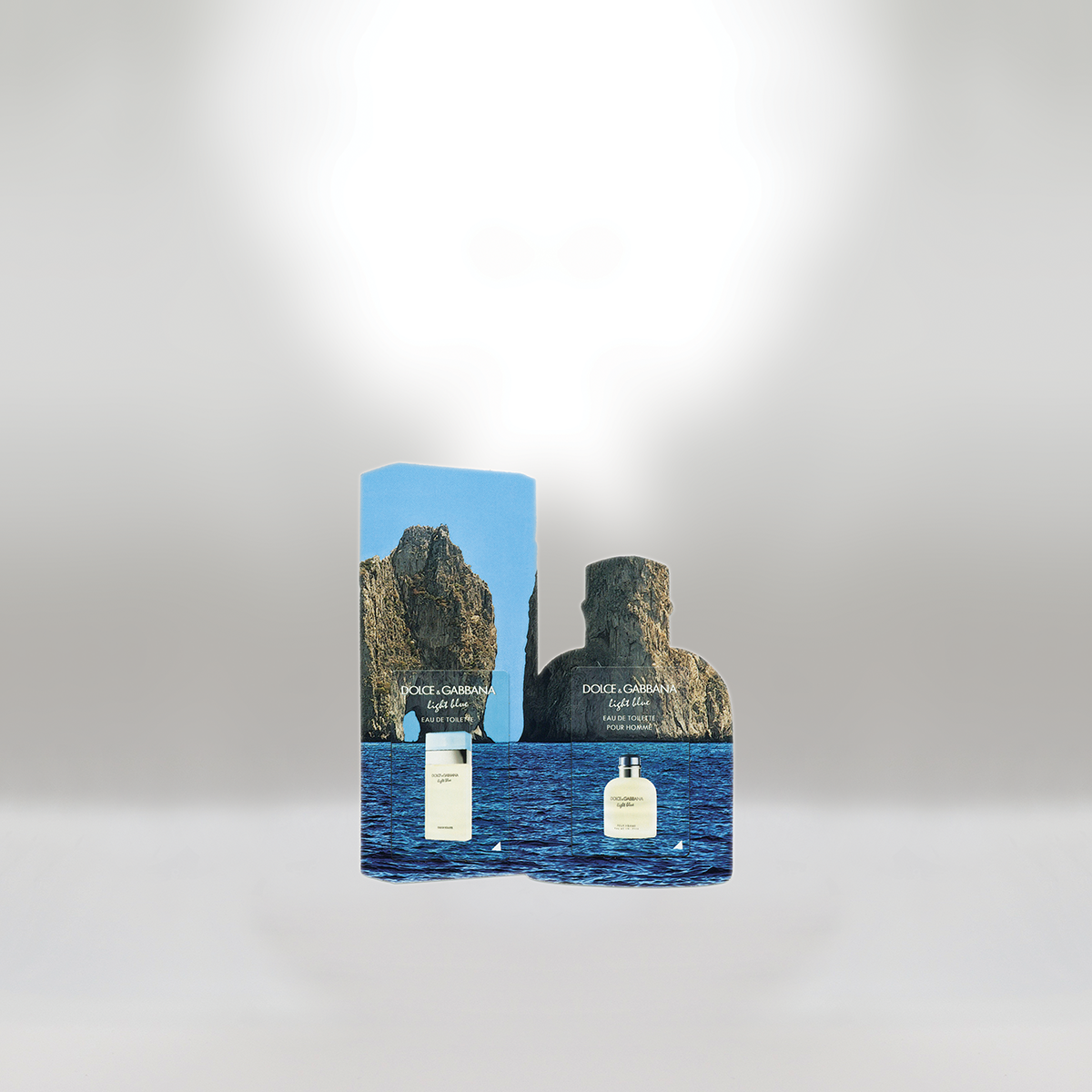 Two Dolce & Gabbana Light Blue perfume bottles, one in front of mountain and ocean scenery, packaging behind showing a similar mountain scene.