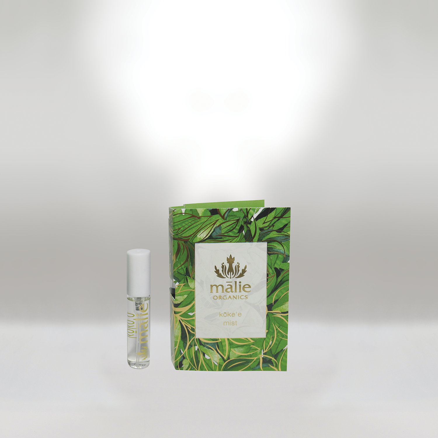 A small clear roller bottle with a white cap, labeled 'mālè', and a green leaf-designed box labeled 'mālè ORGANICS kōke'e mist' against a plain white background.