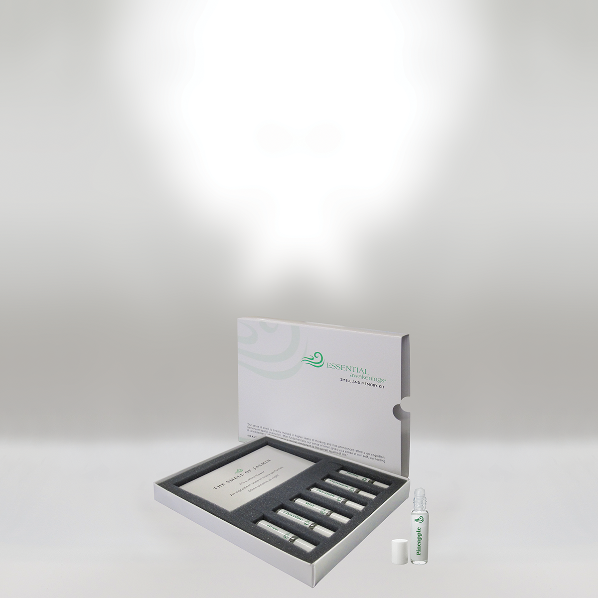 A white box labeled 'Essential Awakenings Smell and Memory Kit' containing six small bottles and an explanatory card, with one bottle outside the box labeled 'Pineapple'.
