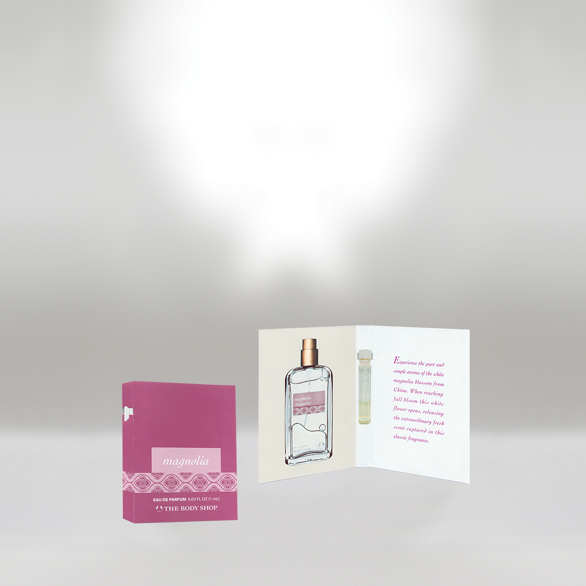 Pink and white box of Magnolia perfume from The Body Shop next to a folded pamphlet. The pamphlet shows an image of a perfume bottle and a floral scent description.