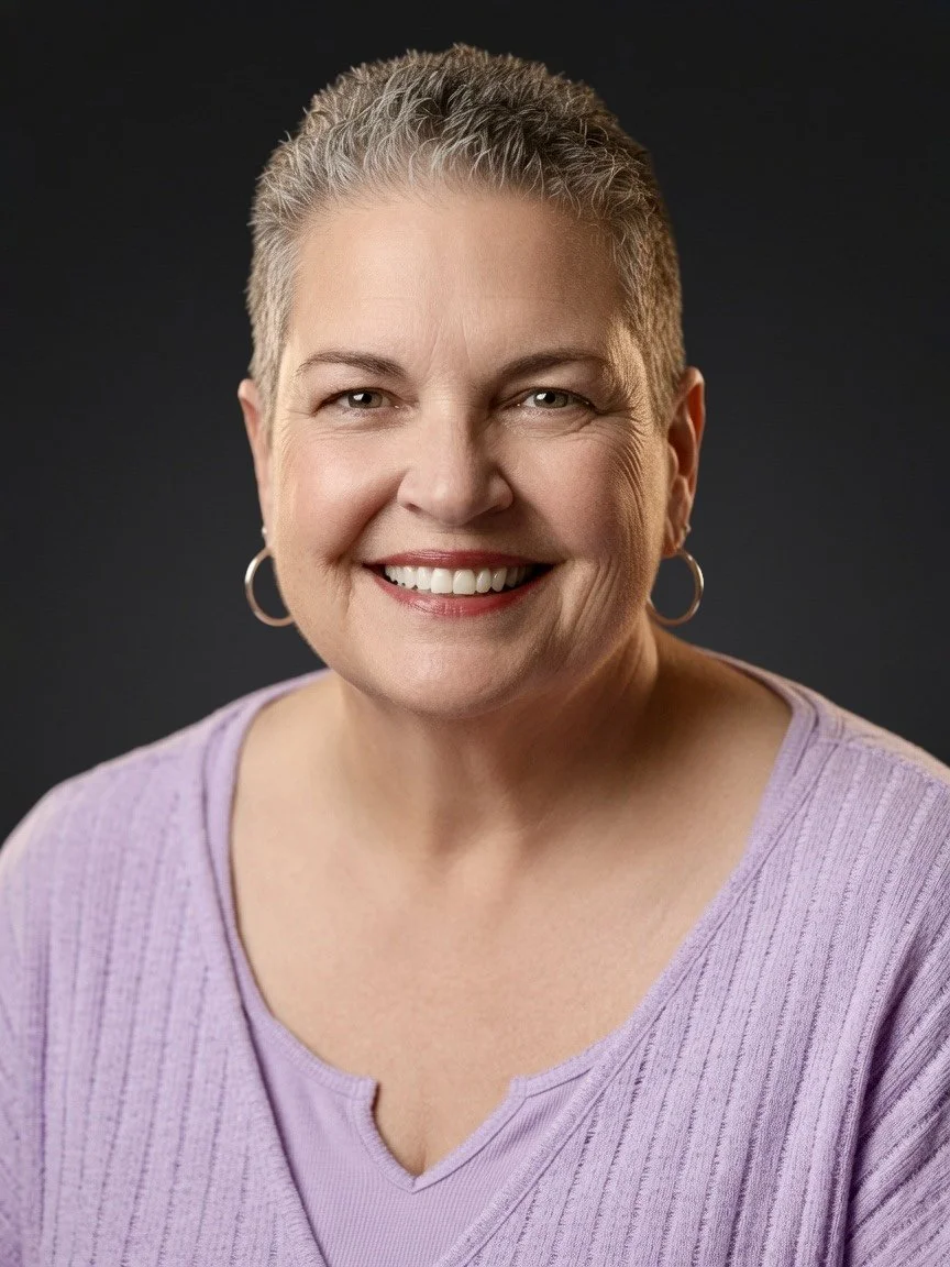 Portrait of a smiling middle-aged woman with short gray hair, earrings, and a lavender top against a dark background.