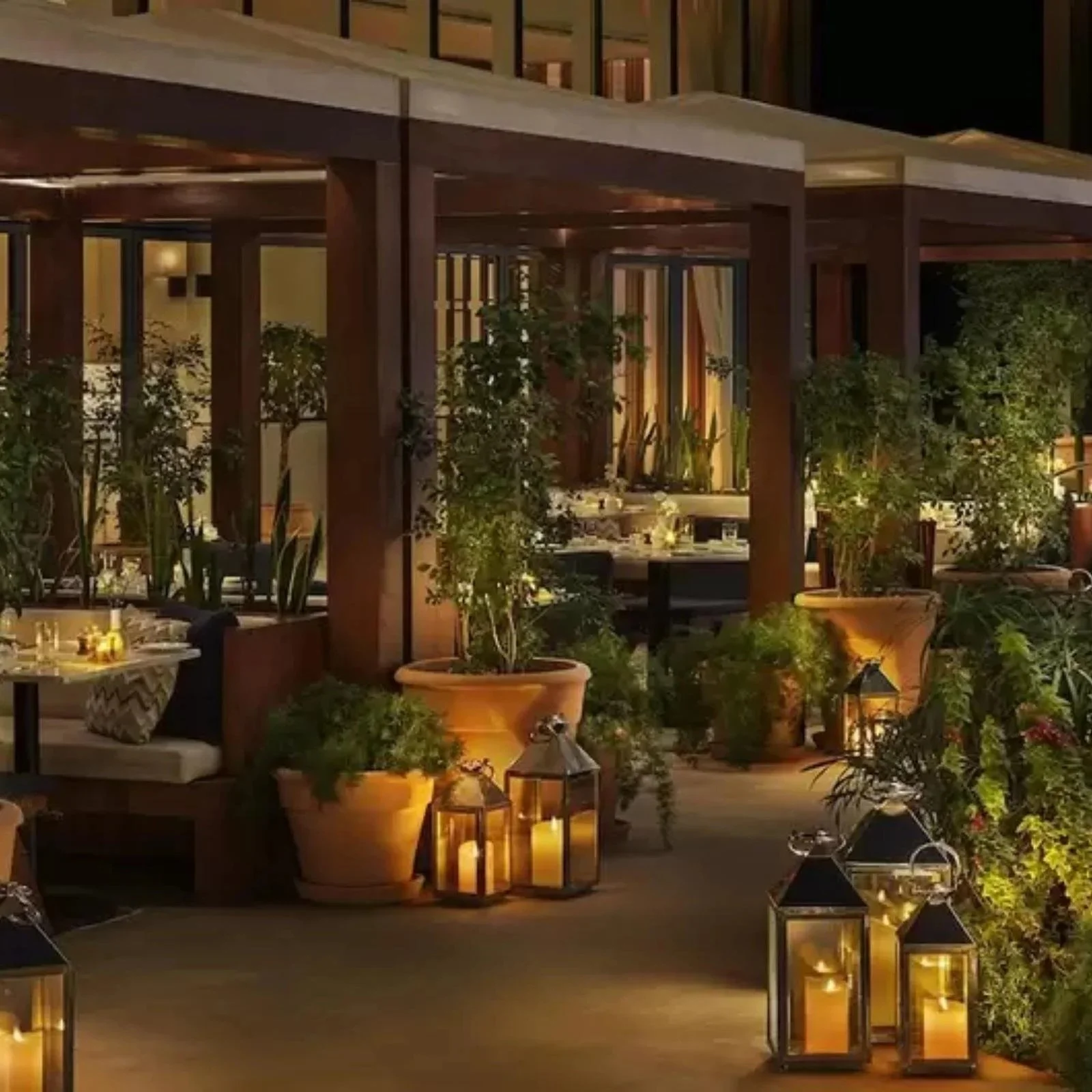 Image of a restaurant patio at night with lanterns glowing and a profusion of potted plants.