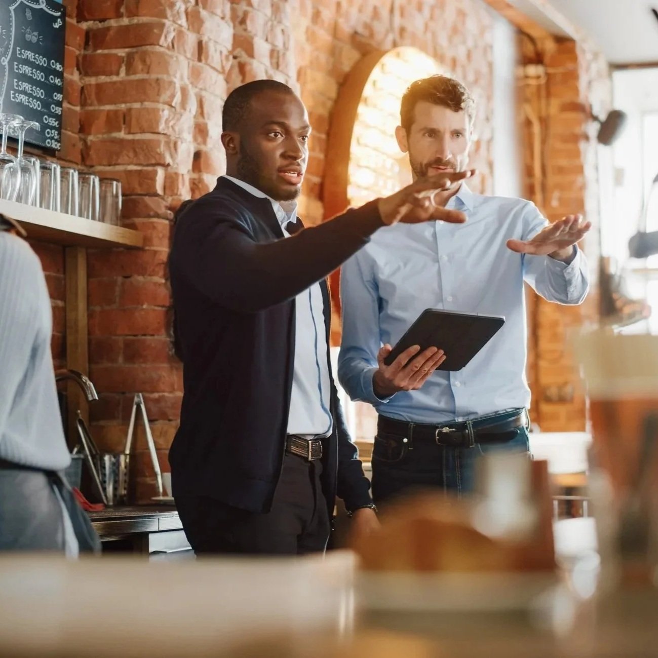 Image of two young men looking at a restaurant both gesturing with a tablet in the right hand of the man on the right