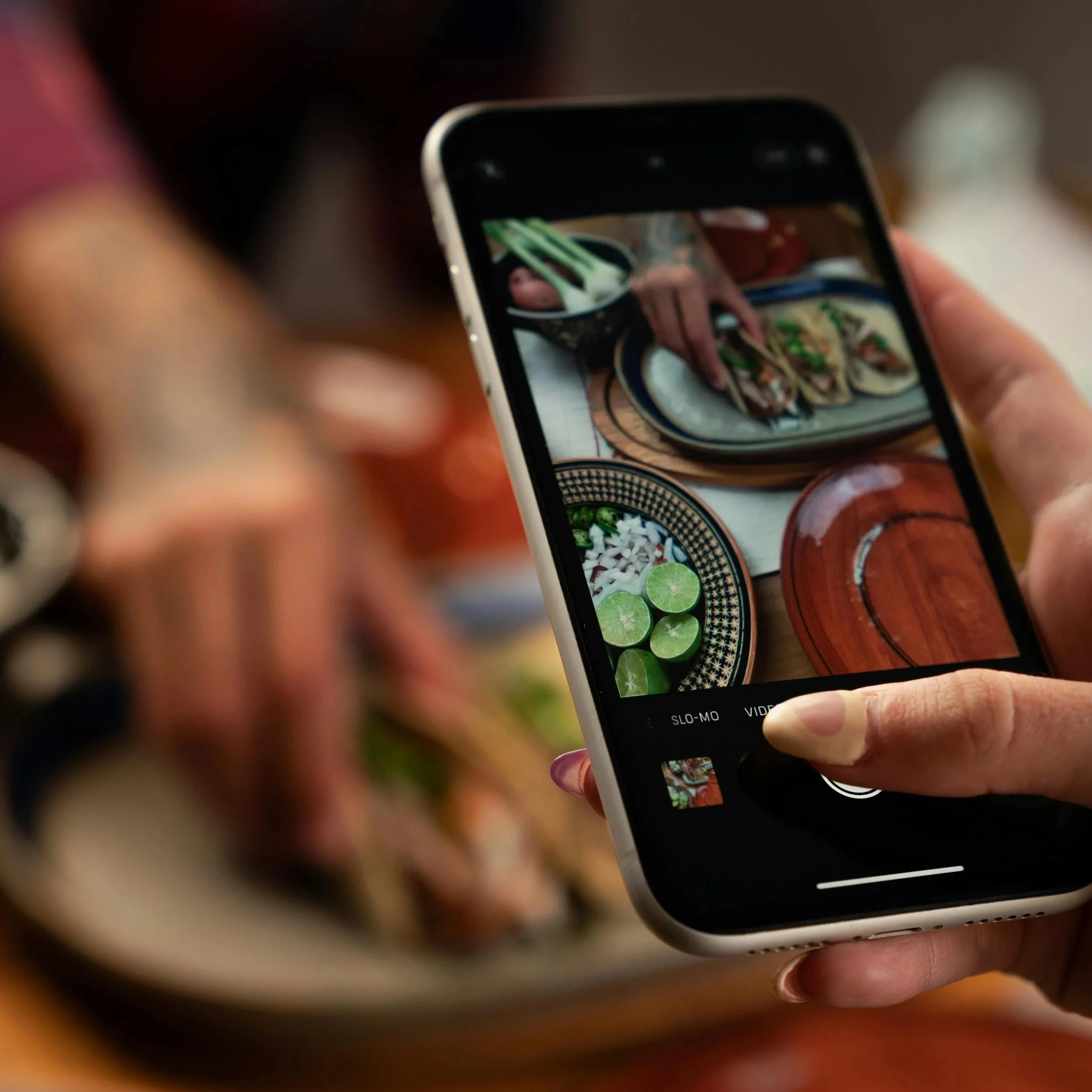 A picture of a woman holding a phone taking a picture of food.