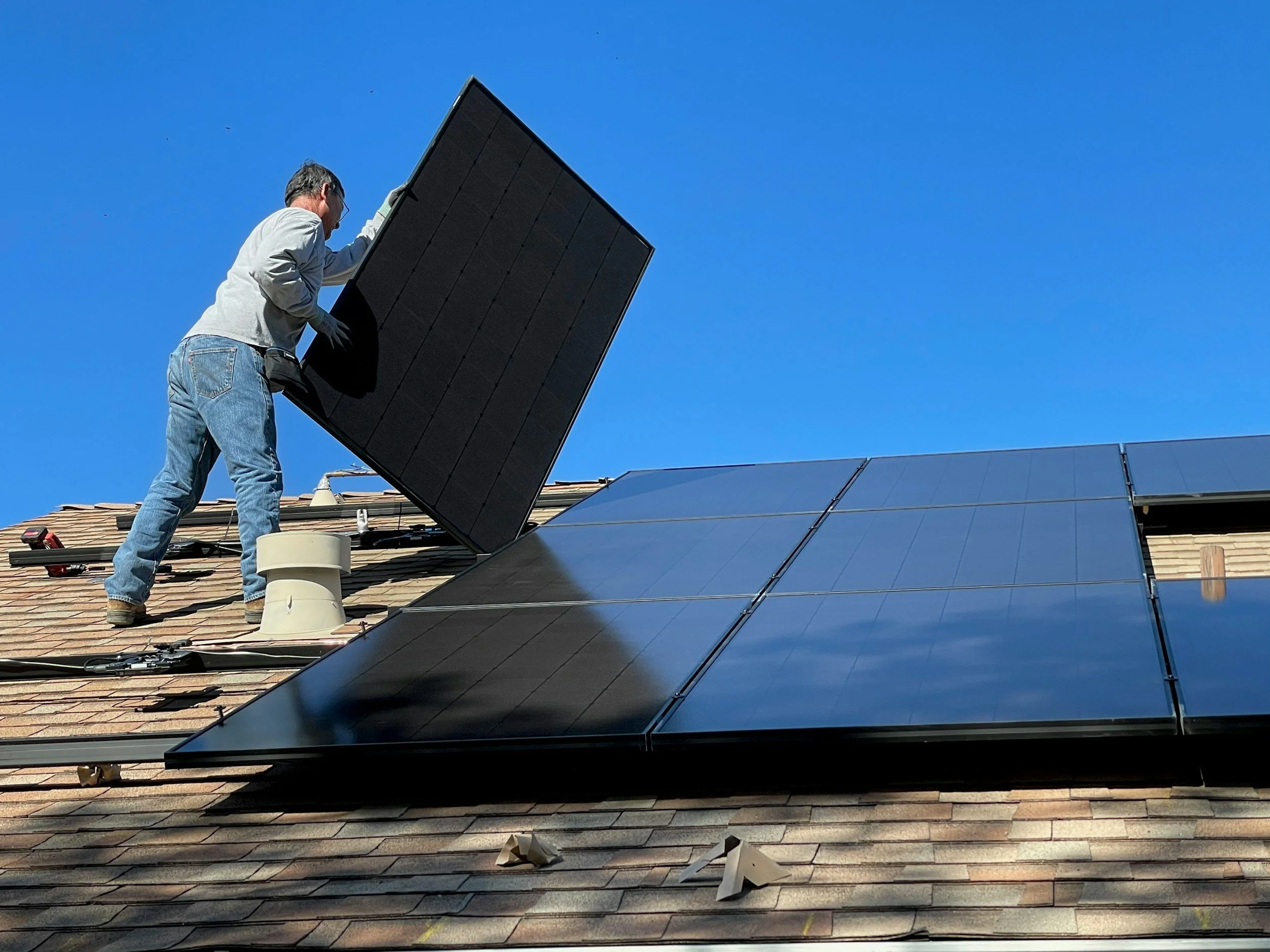 A man installing solar panels on a rooftop under a clear blue sky.