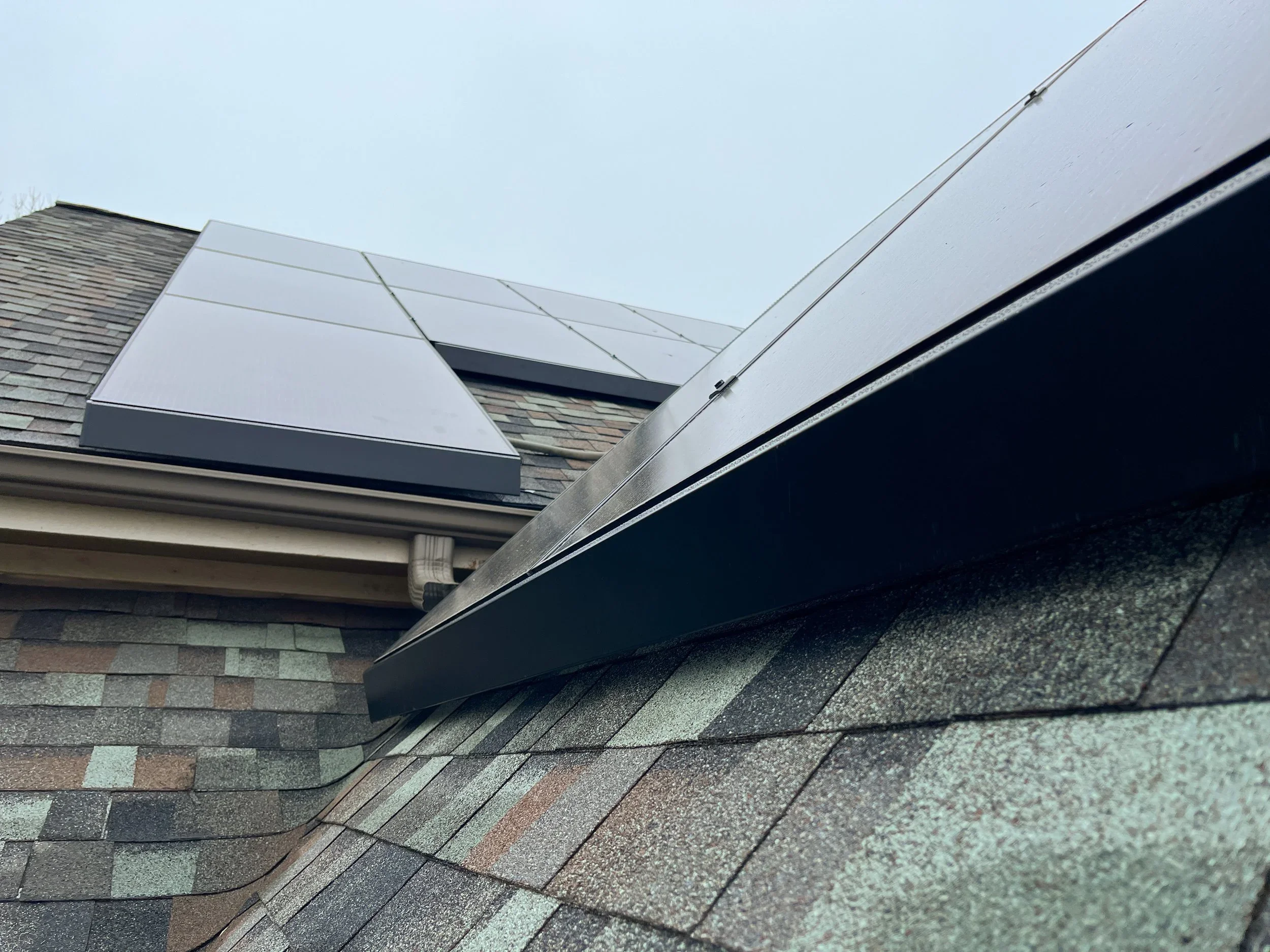 Close-up view of solar panels installed on a house roof with asphalt shingles.