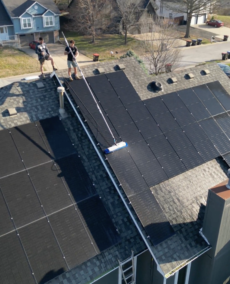 Solar Scapes on a roof cleaning a solar panel with a brush.