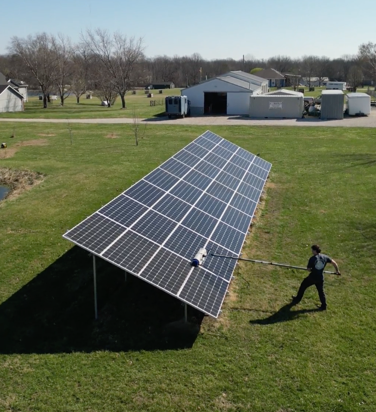 Solar Scapes cleaning a ground mounted solar panel with a brush.