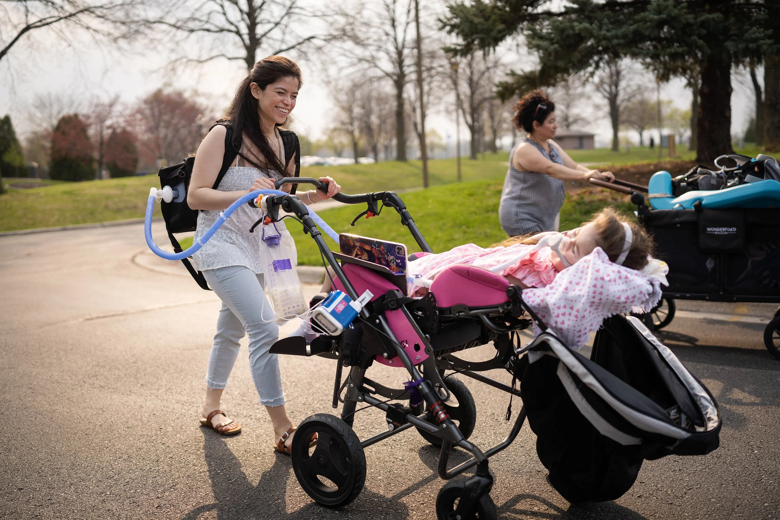 Woman pushing a stroller with a child resting inside at a park during daytime.