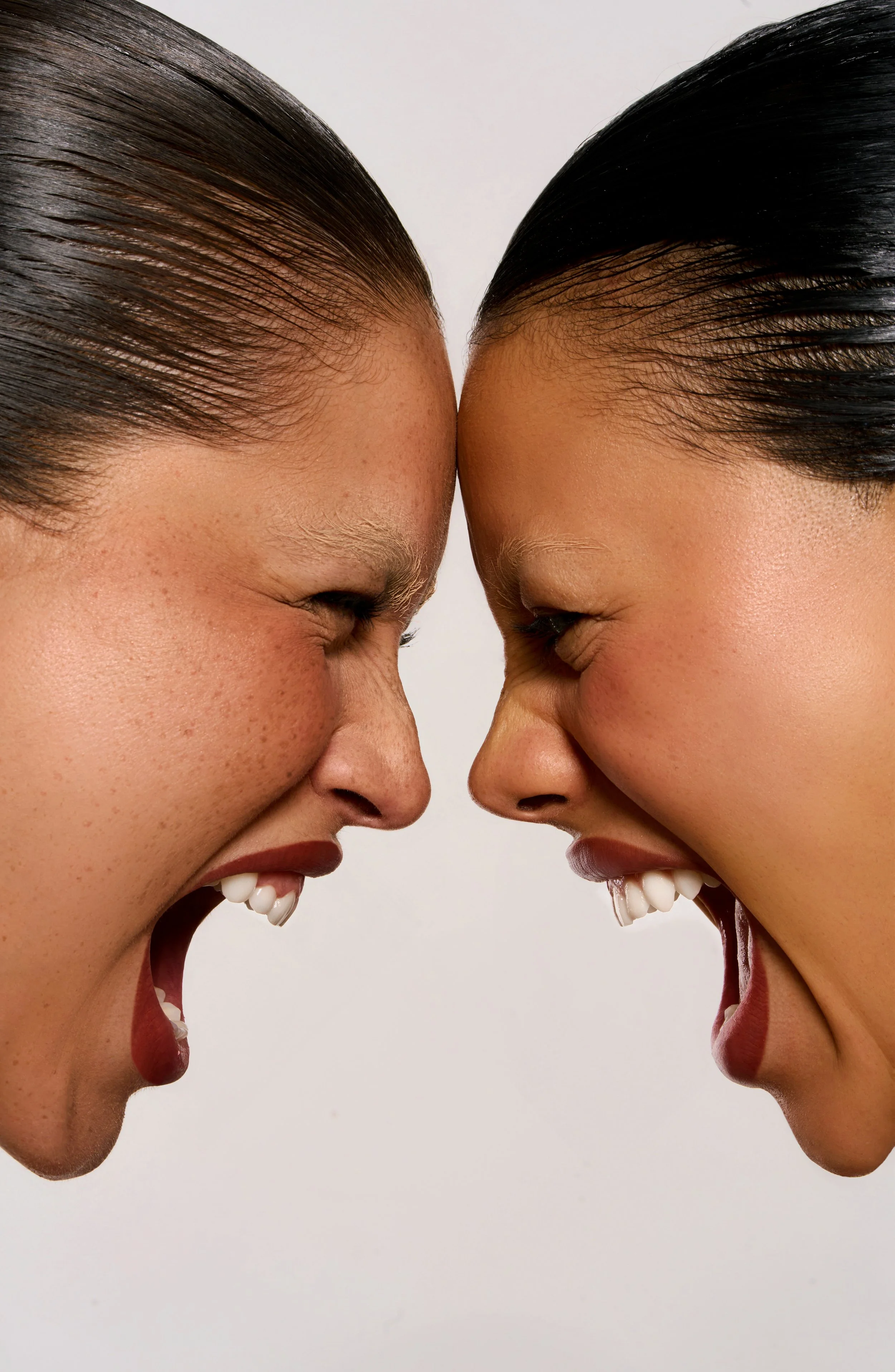Two women with dark hair and light brown skin face each other and appear to be yelling or shouting with intense expressions.