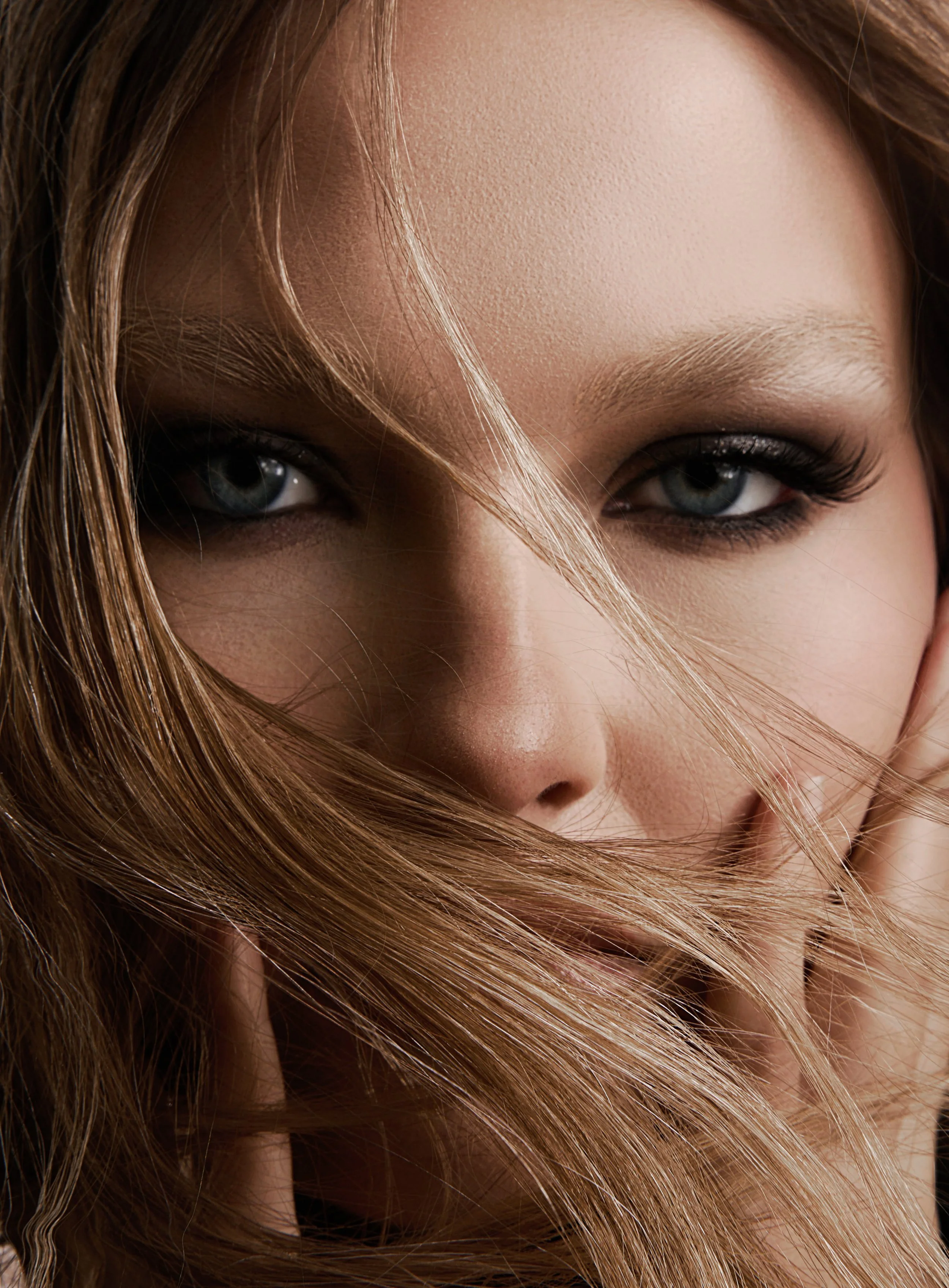 Close-up photograph of a woman's face with striking blue eyes, light makeup, and tousled light brown hair partially covering her face.