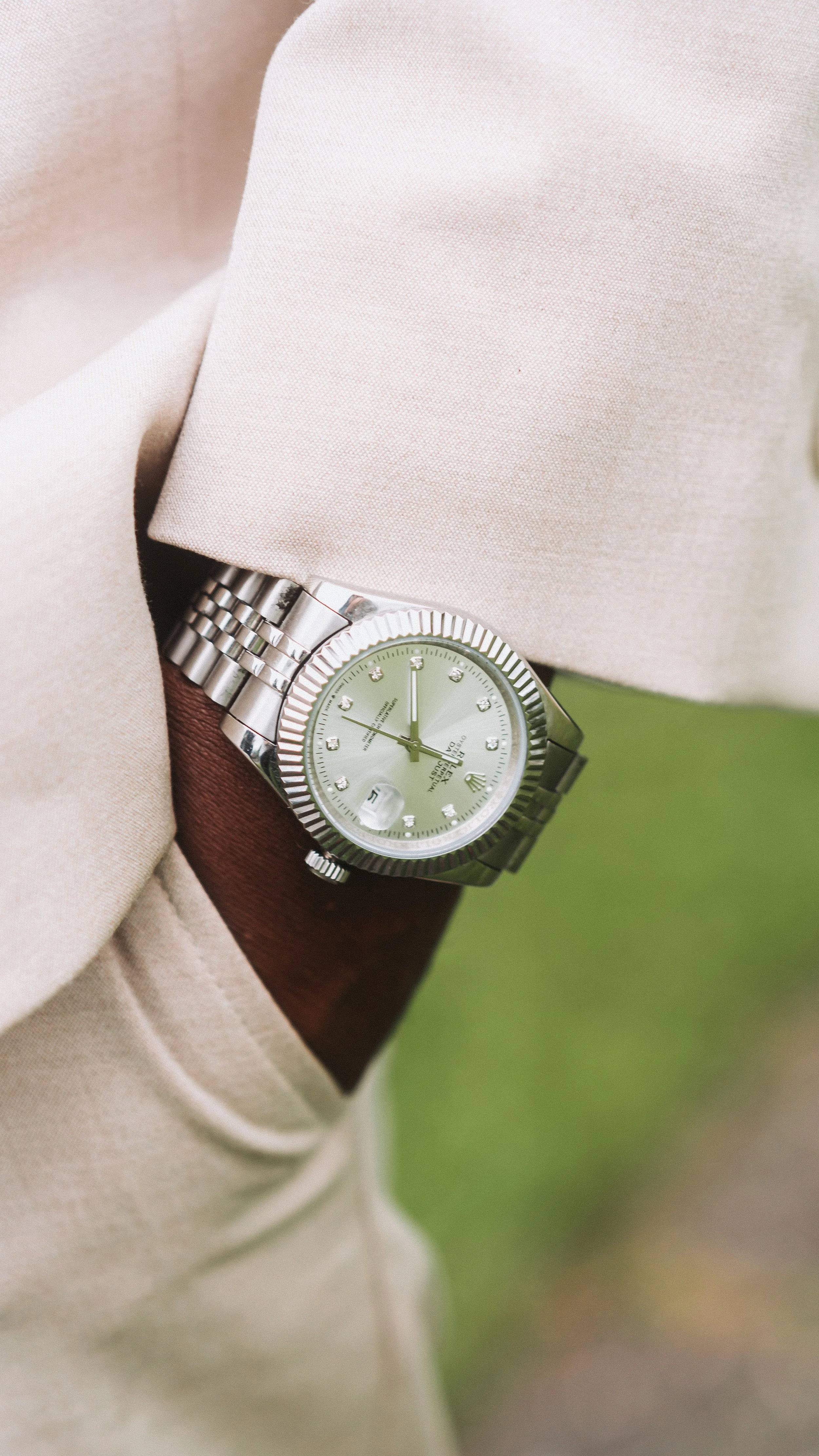 A wristwatch with a silver band and a green dial on a person wearing beige clothing.