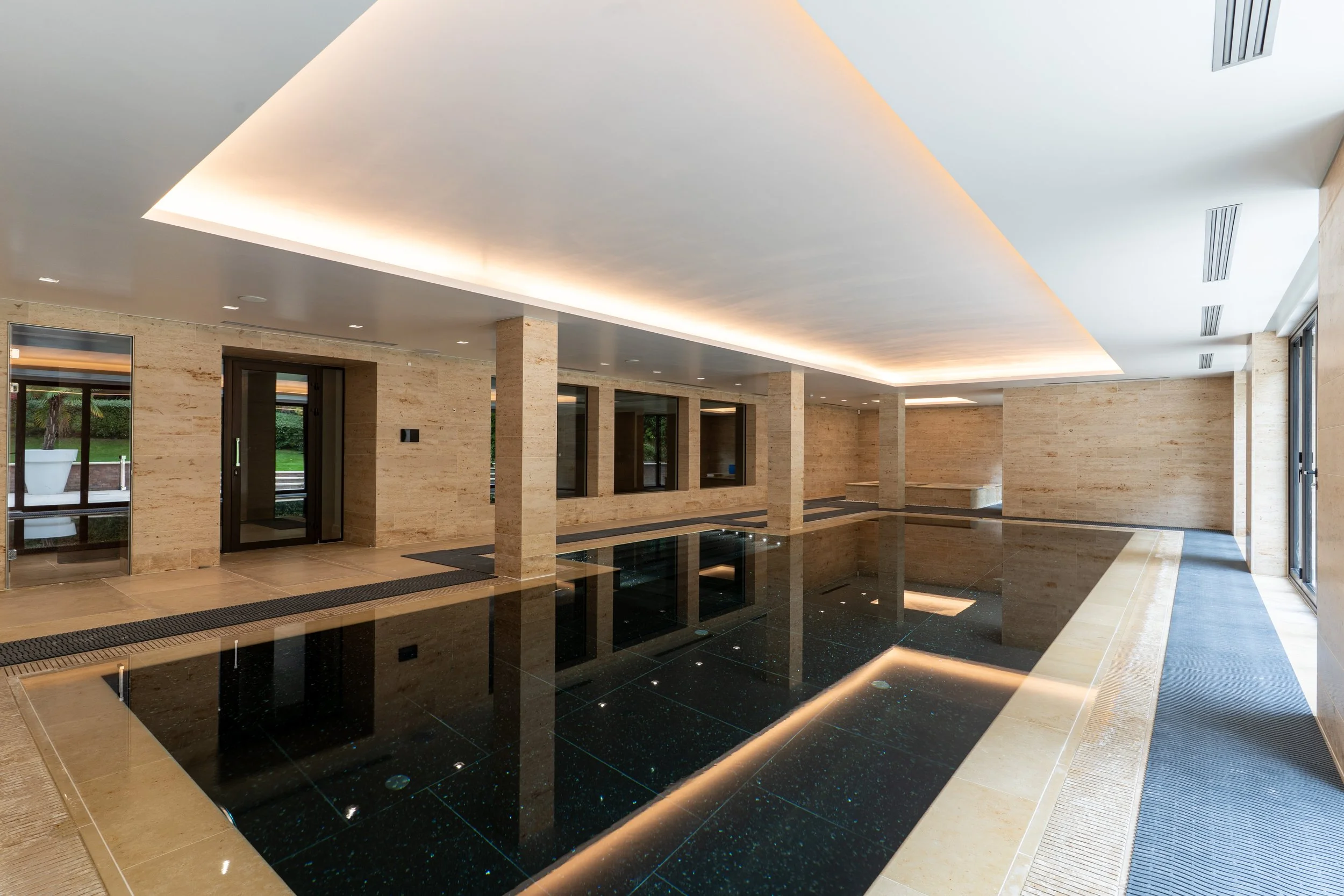Lobby area with beige stone walls, black reflective floor, and a ceiling with integrated lighting.