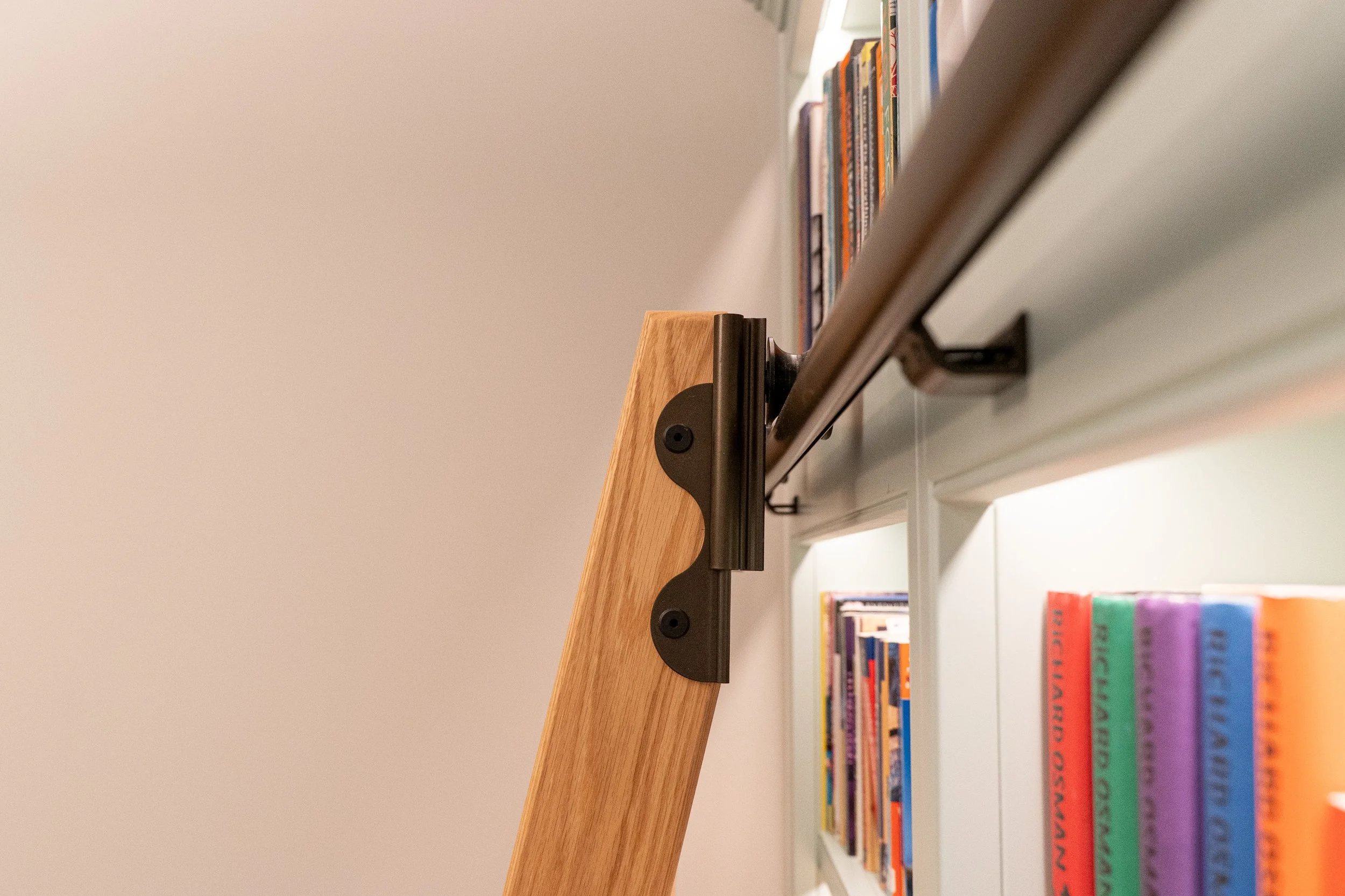 Close-up of a wooden and metal bookshelf support bracket attached to a white shelf filled with colorful books.