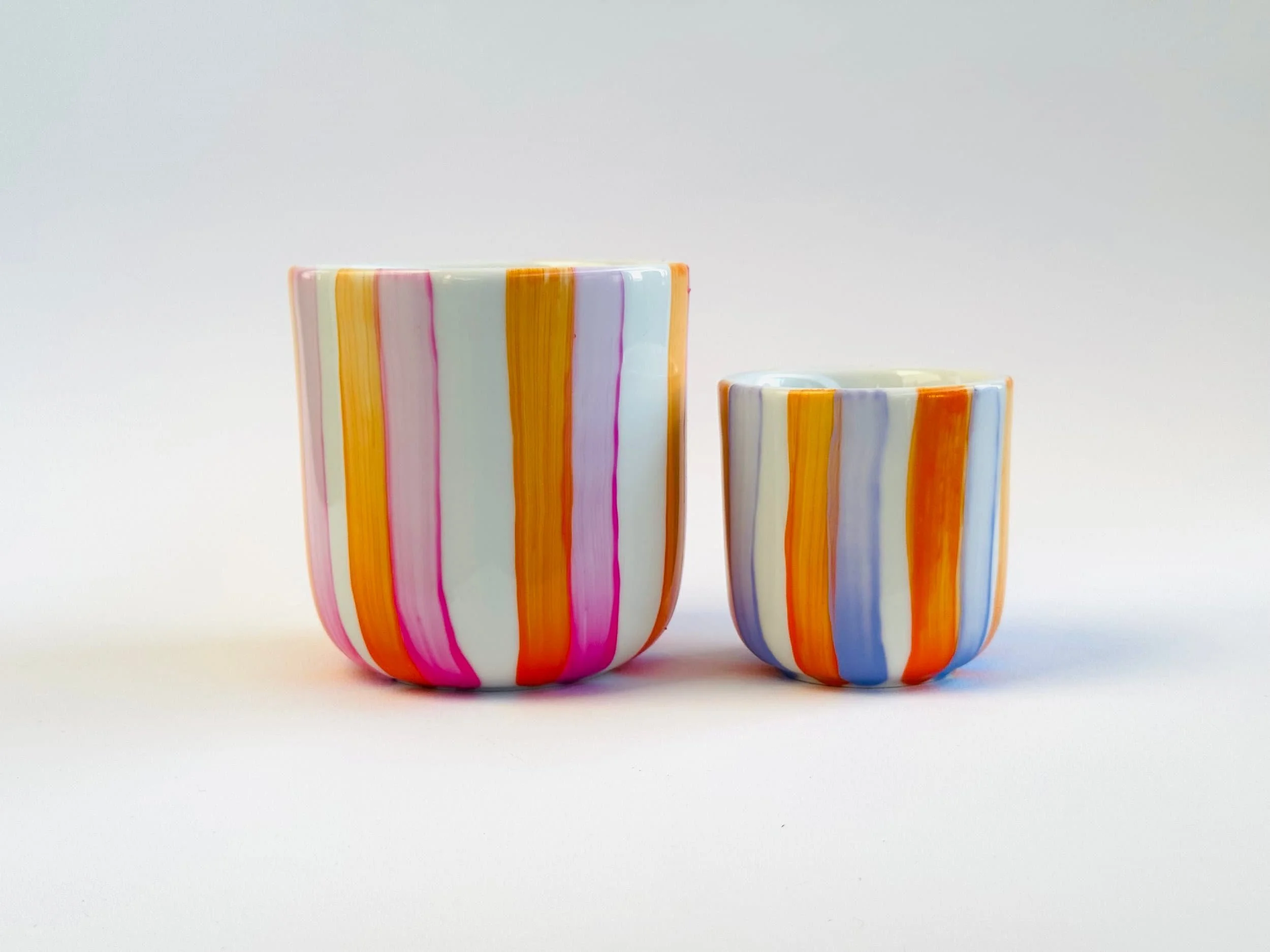 Zwei bunte Keramikvasen mit vertikalen Streifen in Gelb, Orange, Pink, Blau und Weiß auf weißem Hintergrund.