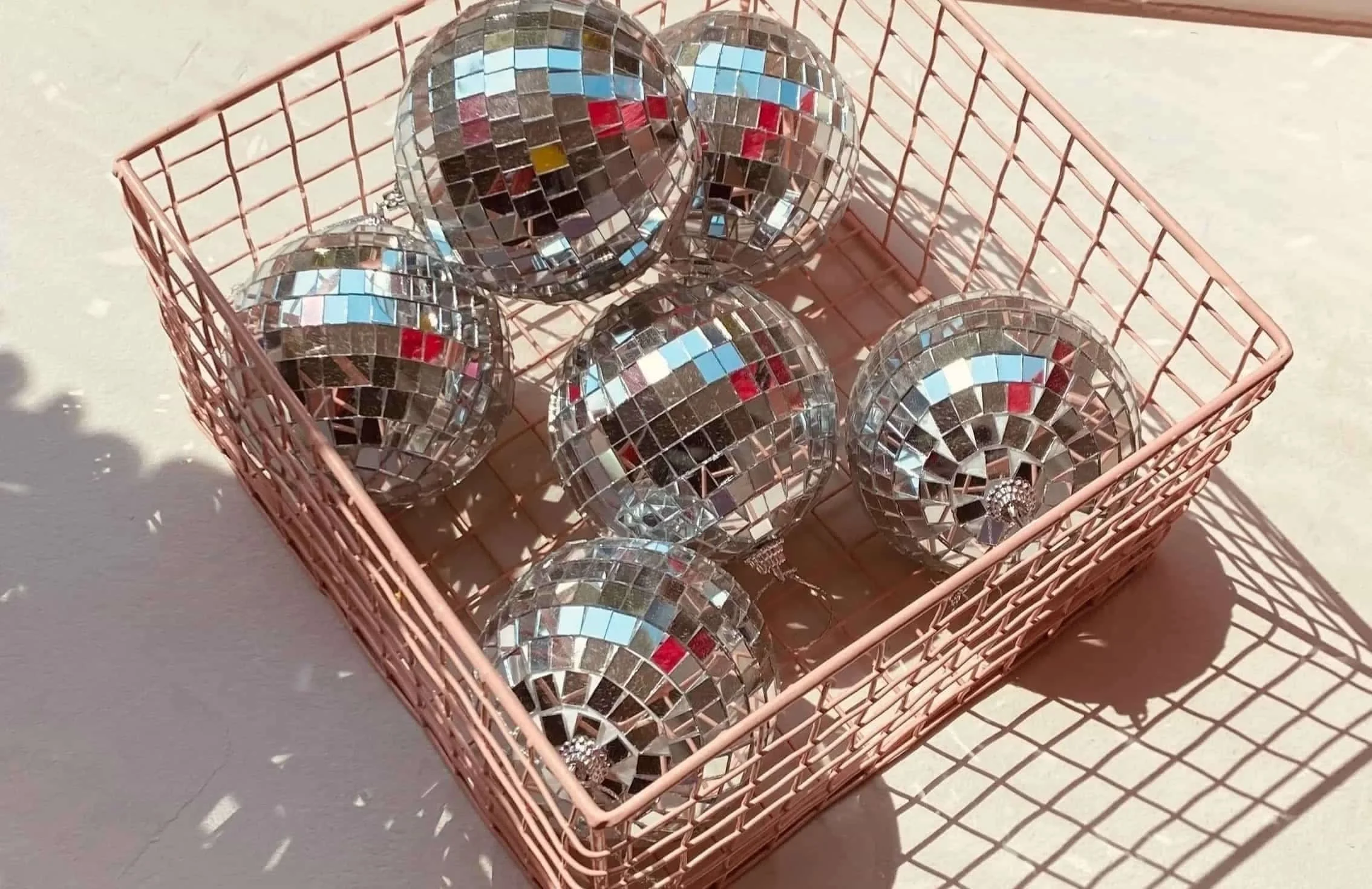 Sechs kleine Spiegelkugeln in einem rosa Korb, auf hellem Untergrund