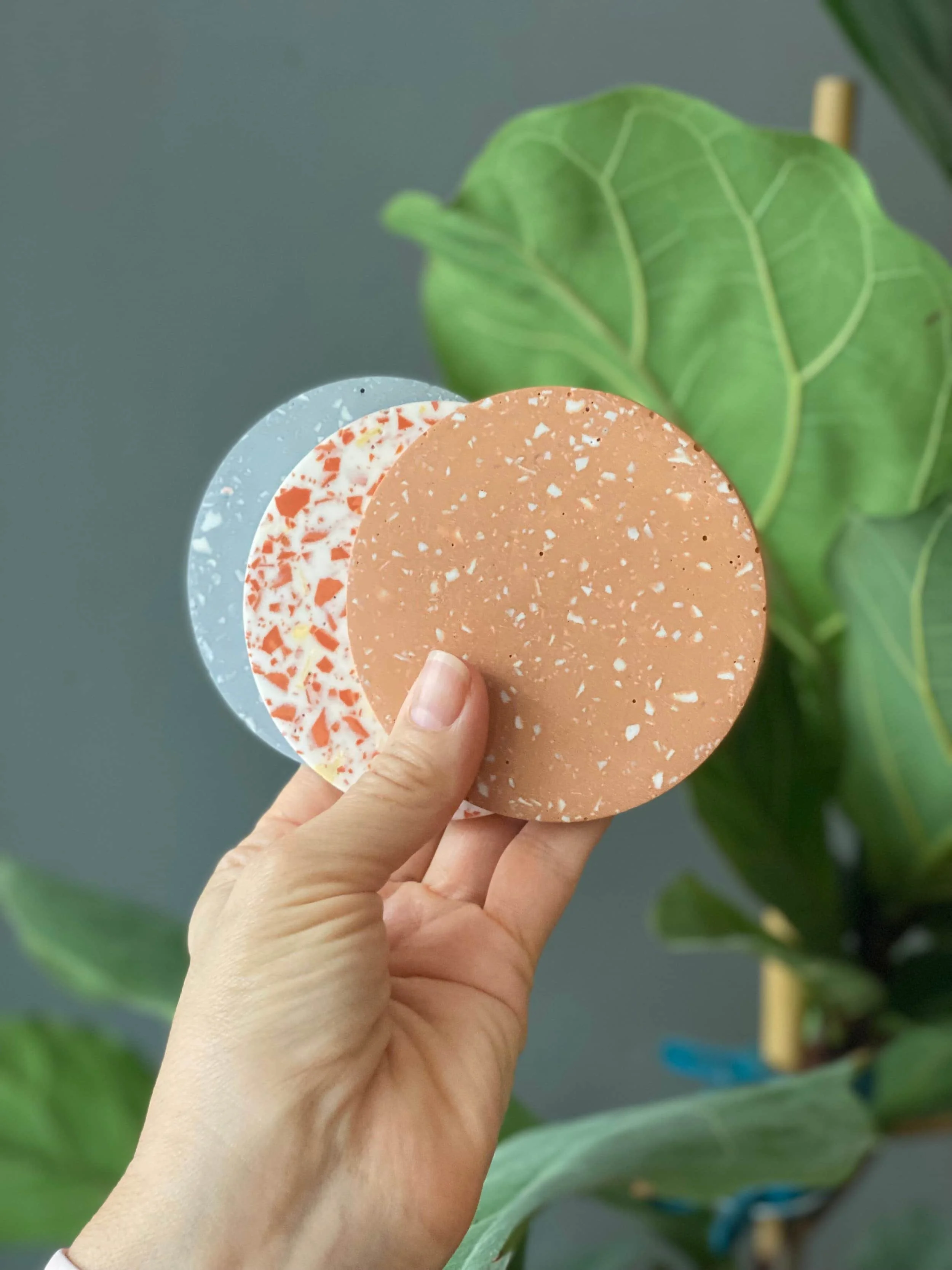 Hand hält drei runde Scheiben in grau mit weißem Terrazzo Muster, in weiß mit Terrakotta Terrazzo Muster, hellbraun mit weißem Terrazzomuster