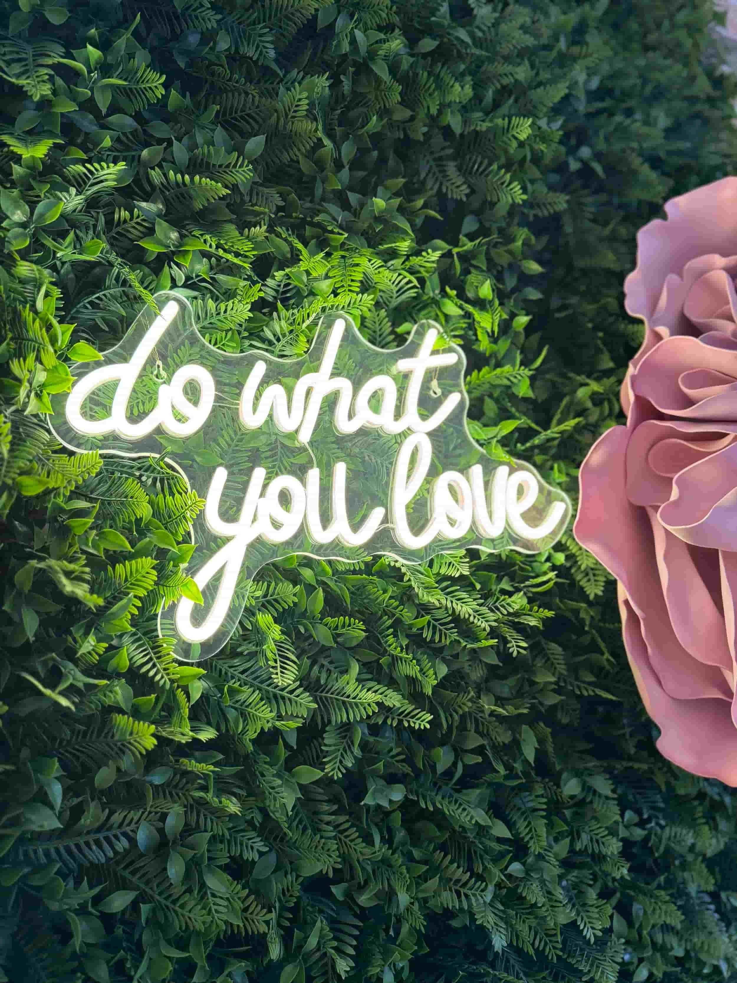 grüner Pflanzenhintergrund mit einer großen rosa Blume sowie der Leuchtschrift von do what you love