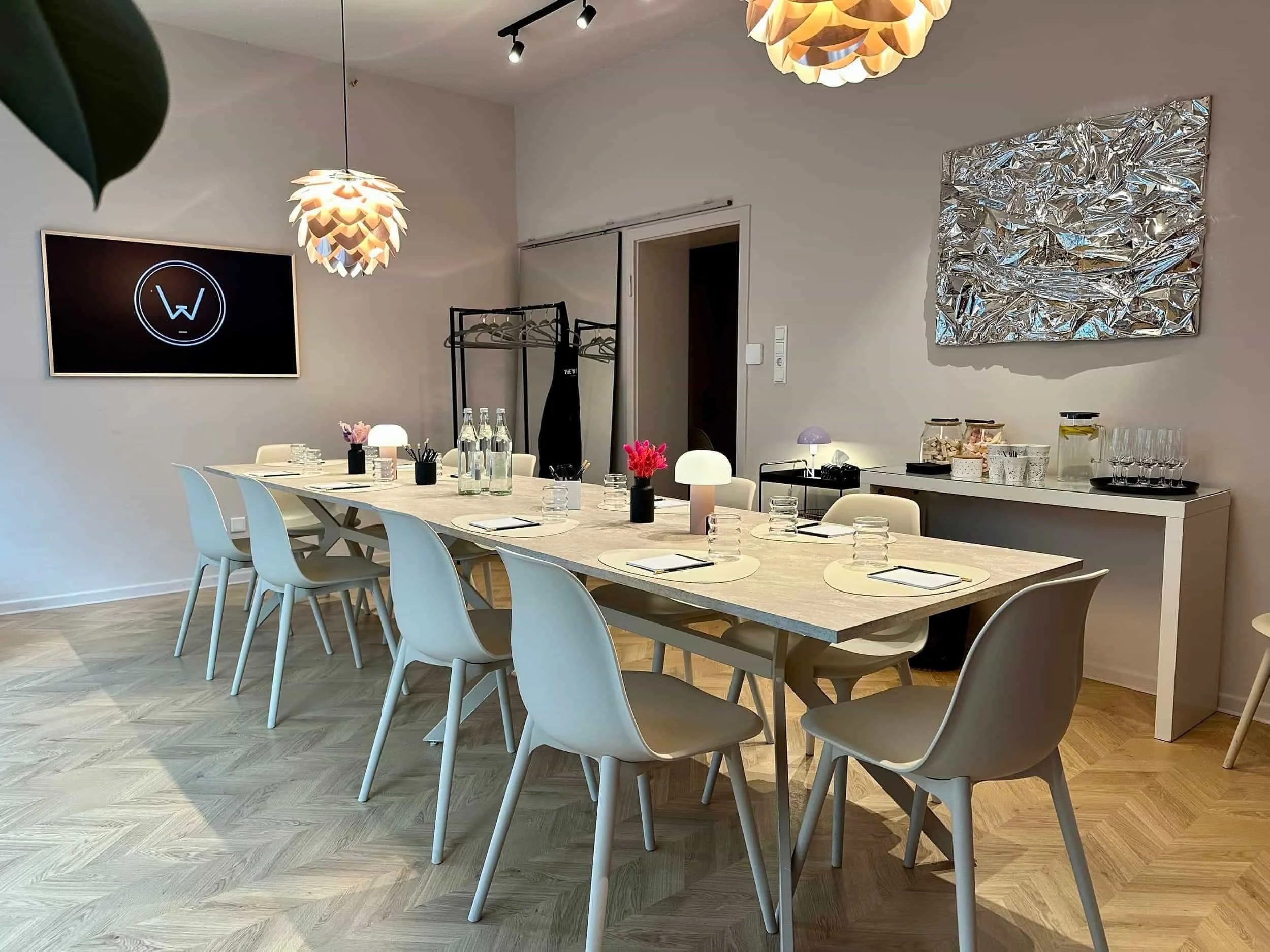 Ein Raum mit Tisch und Stühlen in beige, Fernseher, Hängelampen in Kupfer, Getränke und Gläser stehen im Hintergrund auf einer Konsole