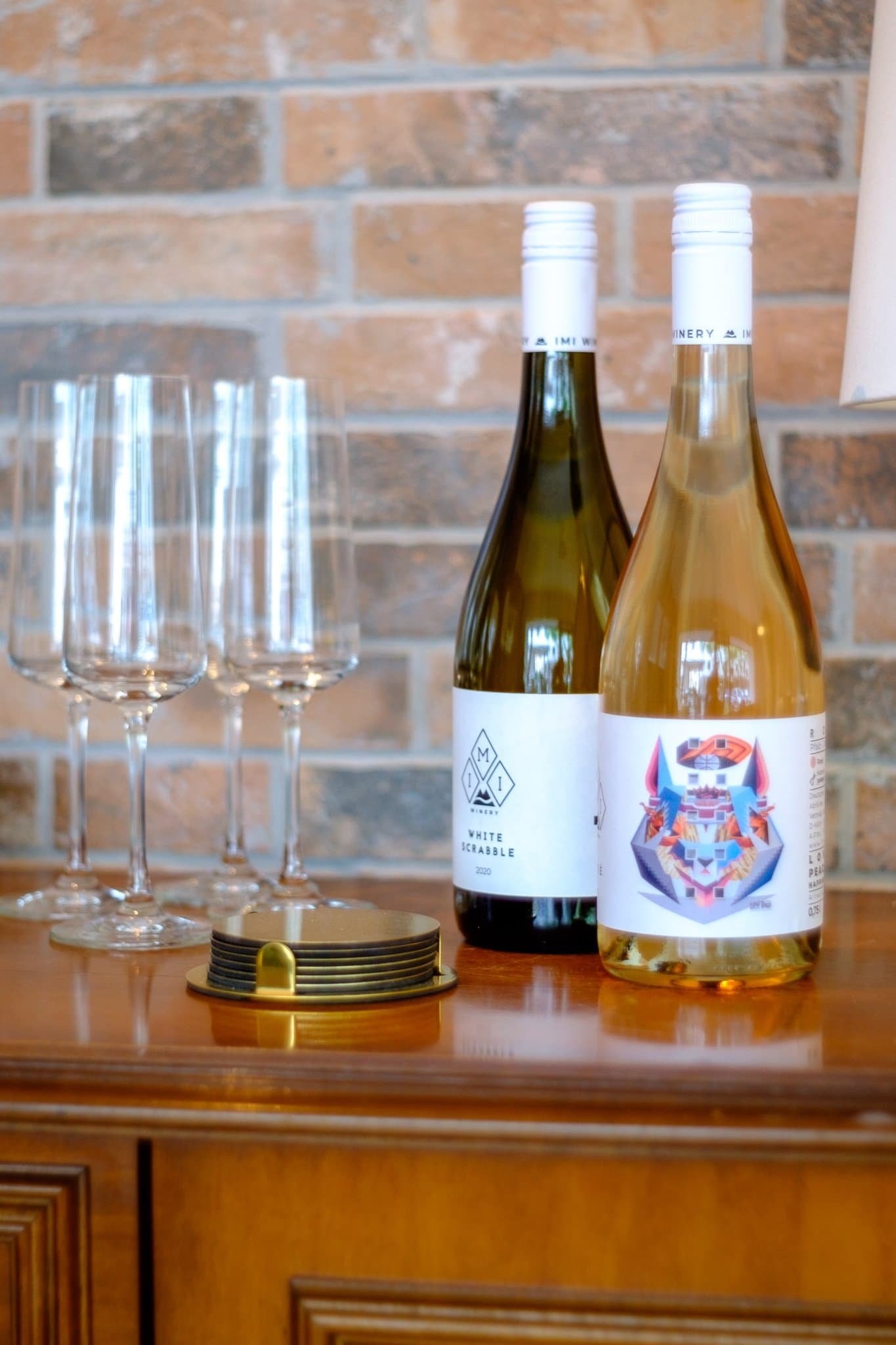 Zwei Weinflaschen und vier Weingläser auf einem Holzsideboard vor einer Ziegelwand.