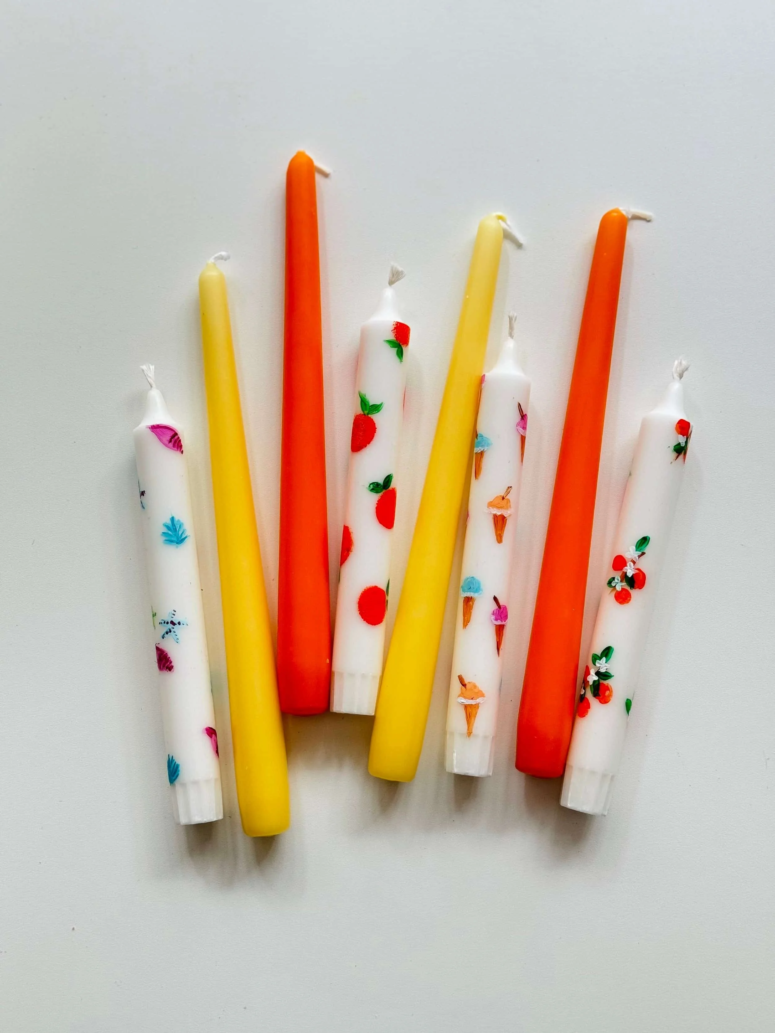 Bunte selbst gemalte Kerzen mit verschiedenen Mustern und Farben auf weißem Hintergrund.