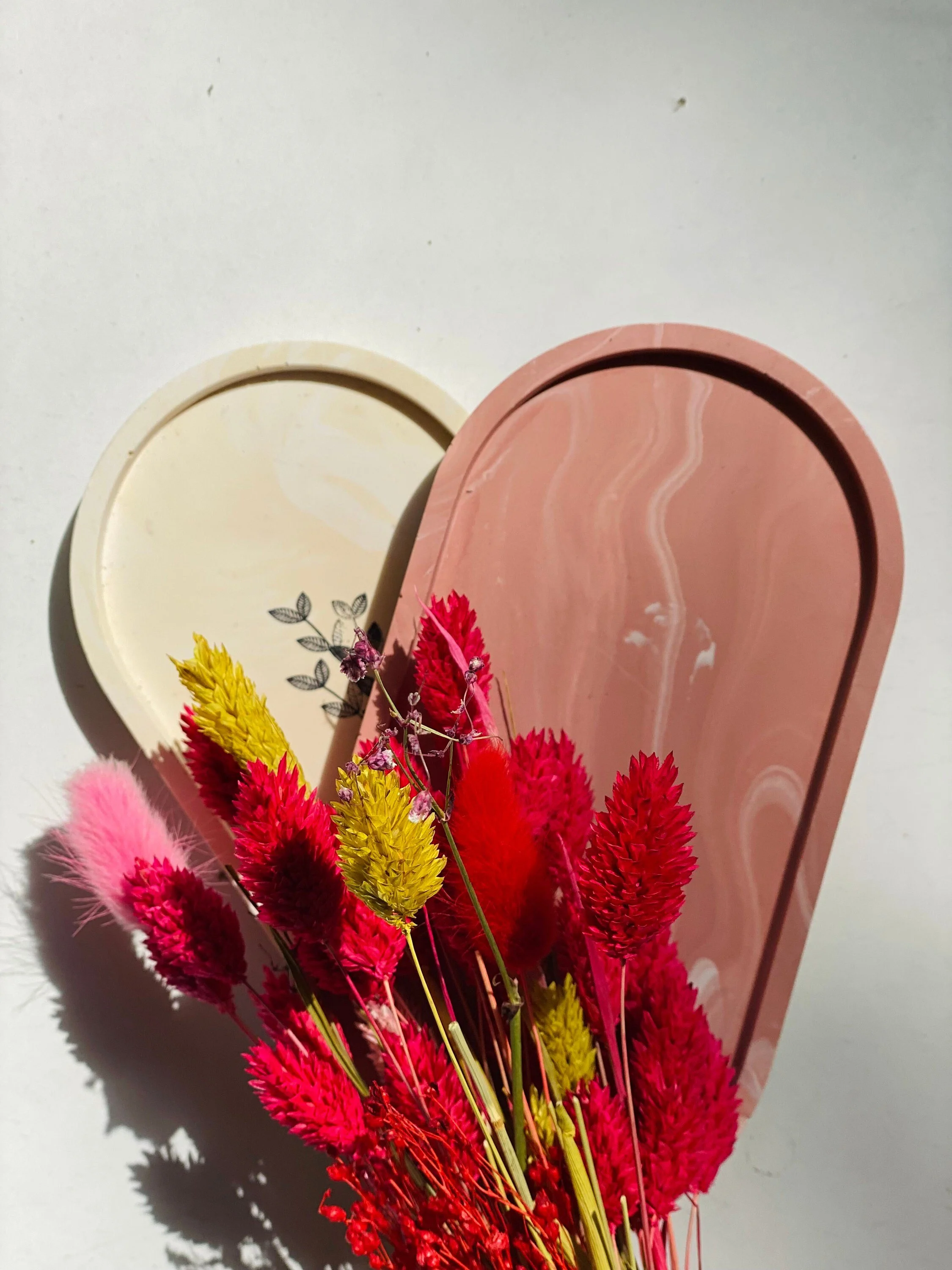 Bunte Trockenblumen in Rot, Pink, Gelb vor bunten Jesmoniteplatten in Rosa und Elfenbein auf weißem Hintergrund.