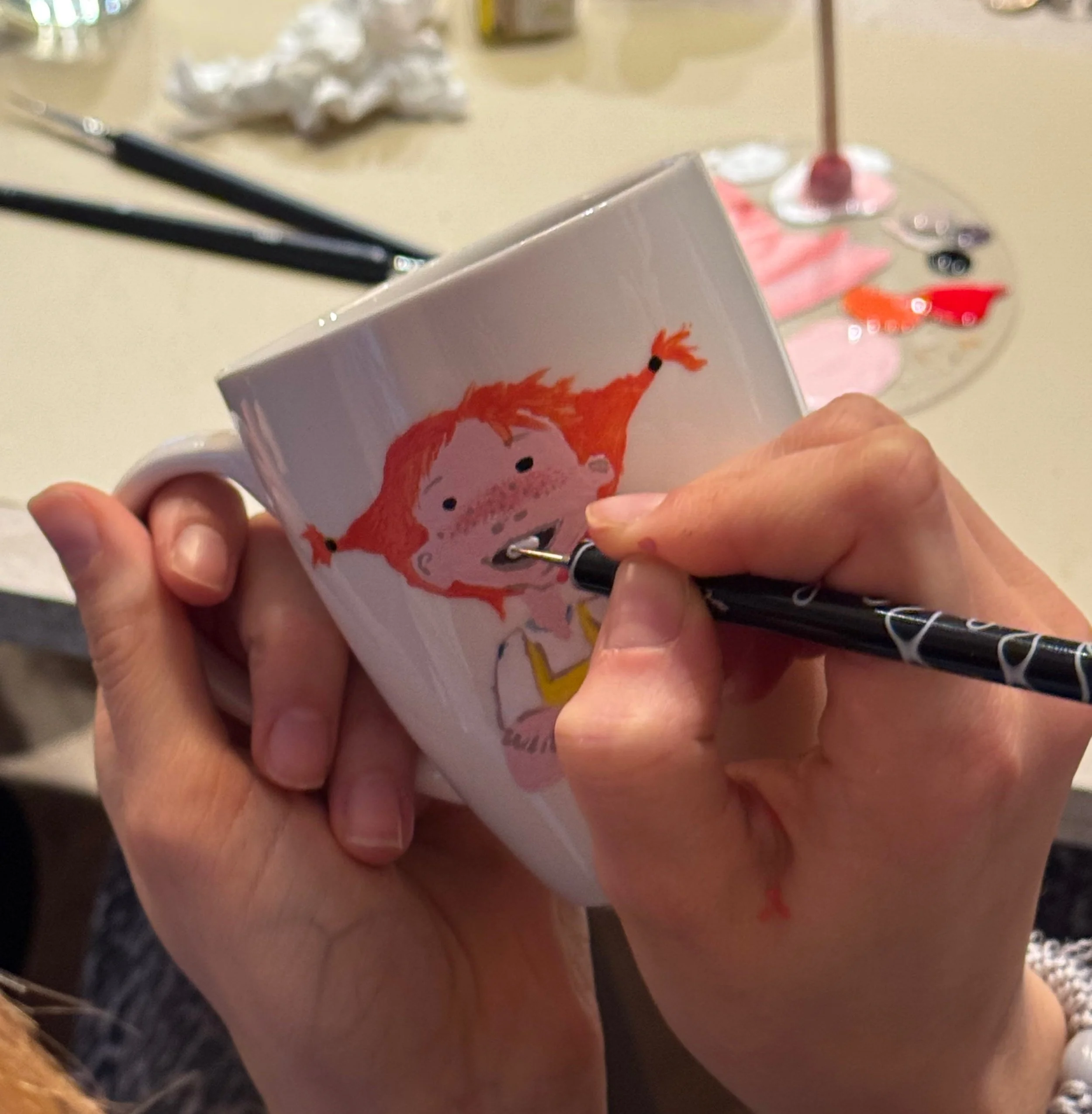 Eine Hand malt Pipi Langstrumpf Motiv auf einer weißen Porzellantasse