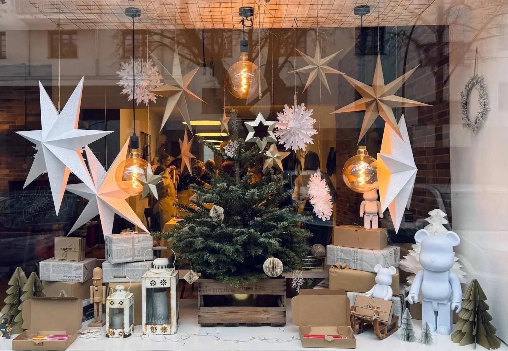 Großes weihnachtlich geschmücktes Schaufenster mit Tannenbaum, großen weißen und braunen Sternen und Schneeflocken hängend von der Decke, weißen Bären, Laternen und kleinen Geschenken