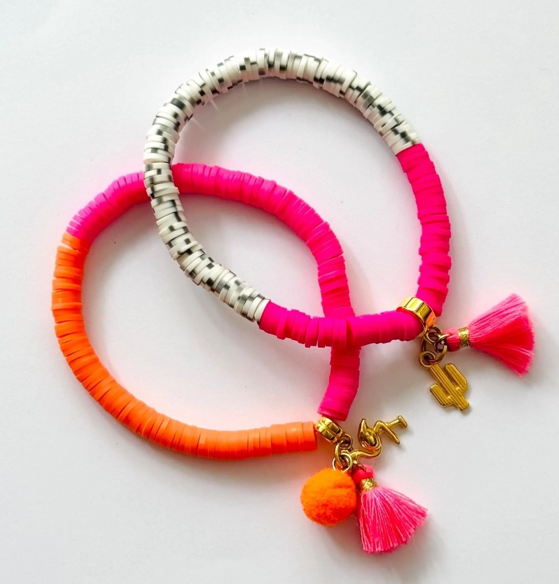 Drei bunte Armbänder mit Charm-Anhängern, Quasten und Perlen in Pink, Orange, Weiß und Grau