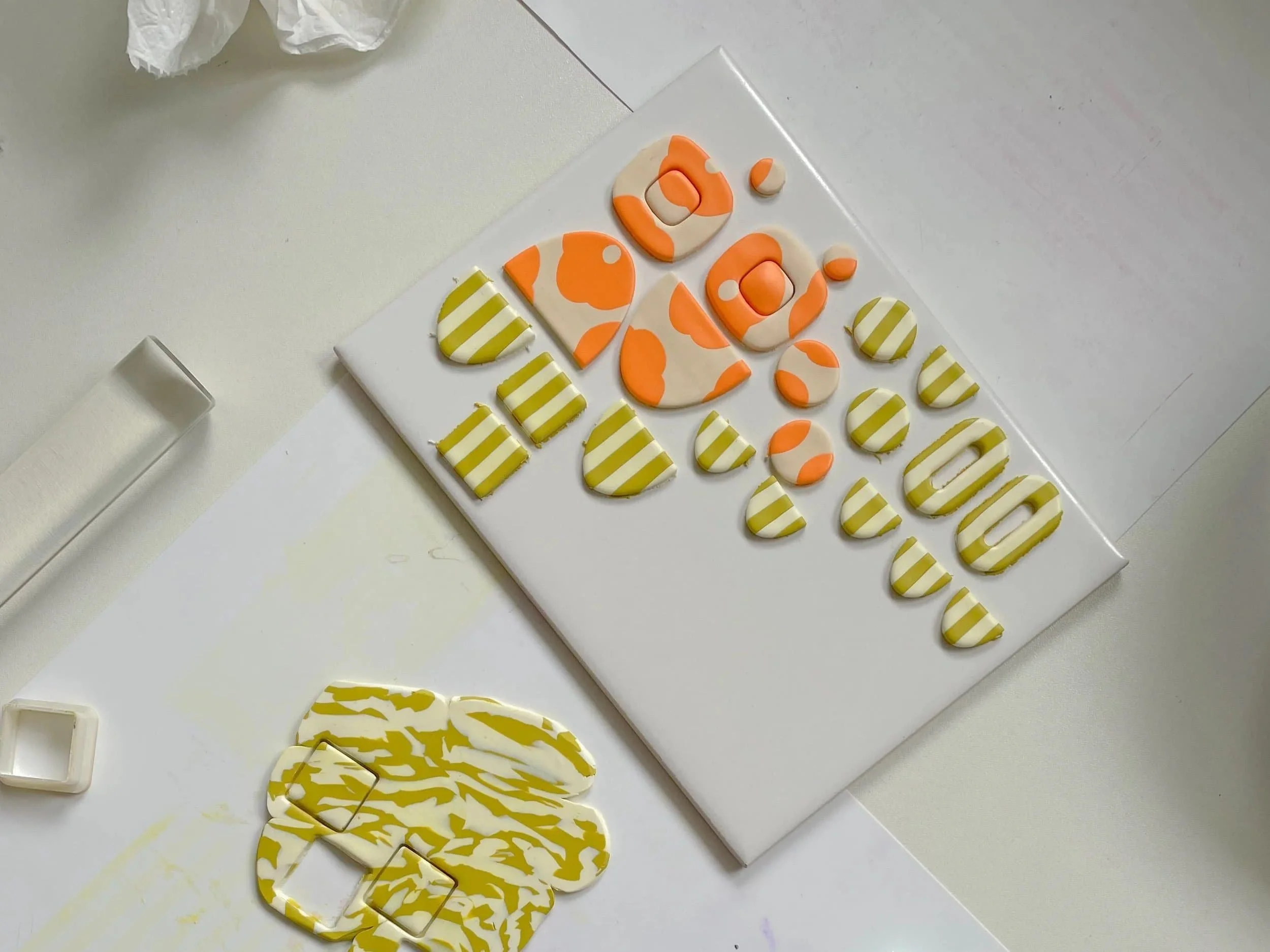 bunte Abschnitte aus Polymer Clay Masse liegen auf dem Tisch neben Acrylroller und anderen Tools