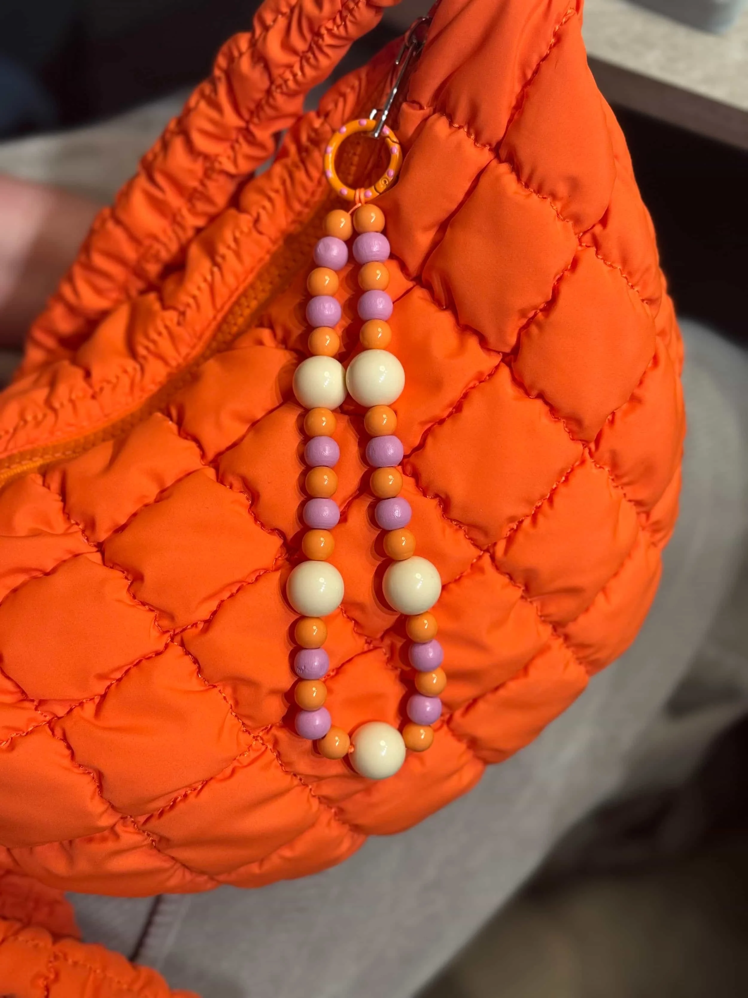Orange gesteppte Tasche mit Schlüsselring und Perlenkette in Pastellfarben zwischen Lila, Orange und Creme. 